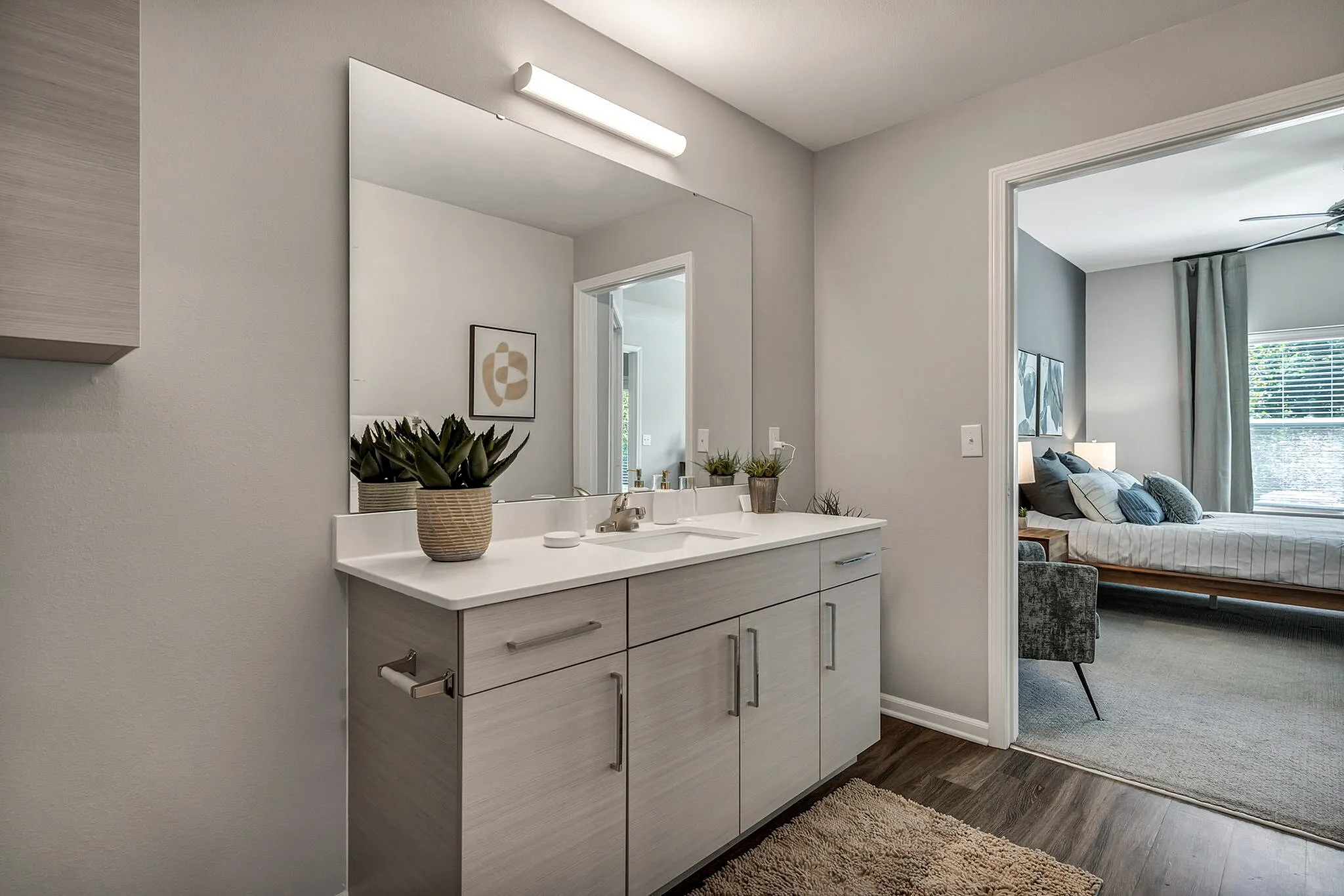 Elegant and modern bathroom with sleek vanity, illuminated mirror, and stylish decor leading into a cozy, sunlit bedroom with tasteful furnishings.