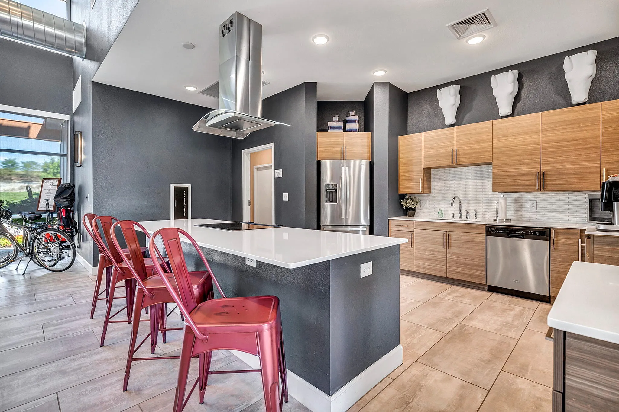Modern kitchen with sleek countertops, stainless steel appliances, and vibrant red bar stools, offering a contemporary look with ample natural light.