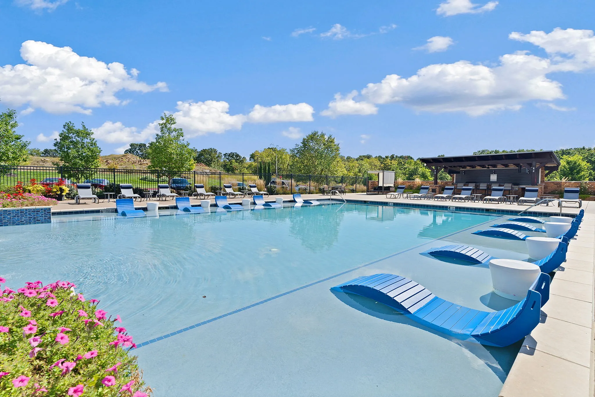 Luxurious outdoor pool with sleek blue loungers, surrounded by vibrant landscaping and open skies, offering a perfect relaxation retreat.