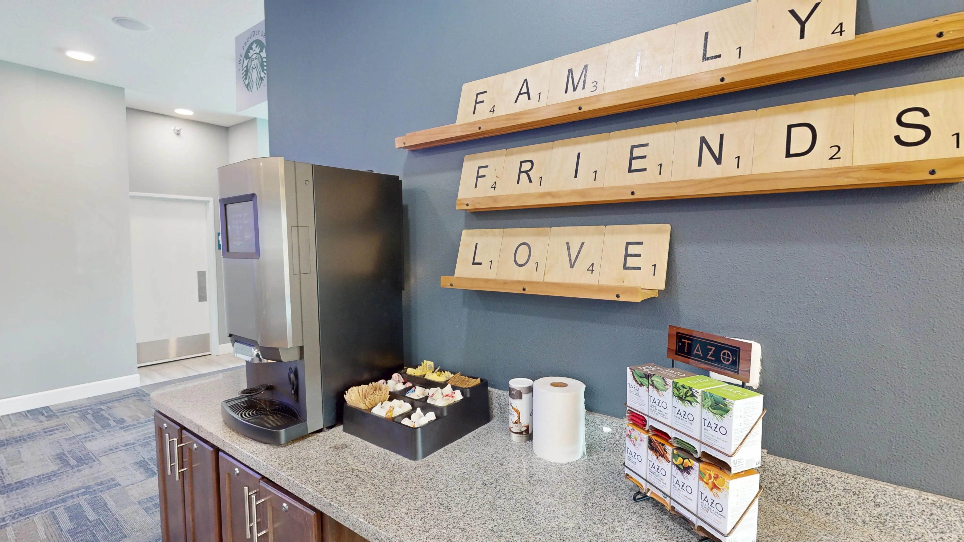 Inviting coffee station with modern decor, featuring motivational Scrabble-style wall art and a selection of Tazo teas.