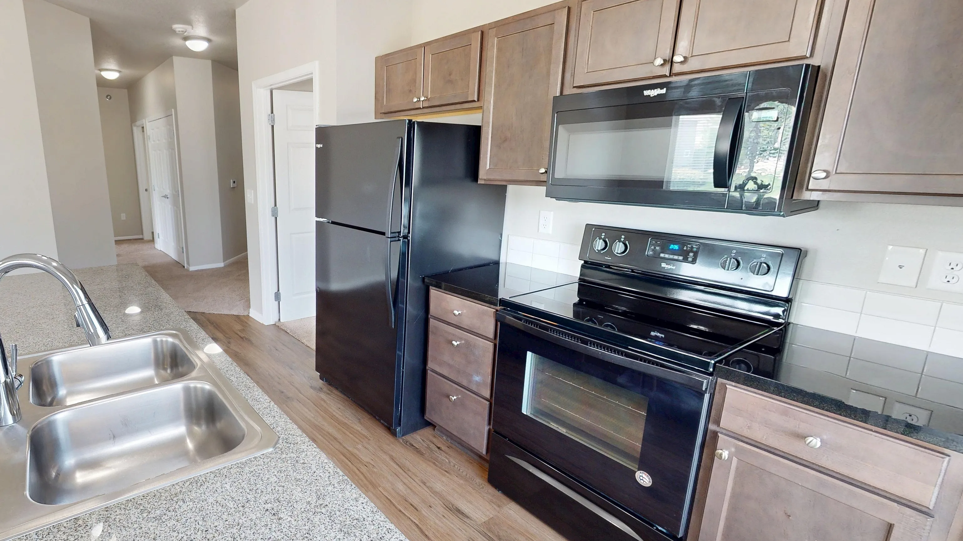 Modern kitchen featuring sleek granite countertops, dual sinks, and contemporary black appliances in a bright open space.