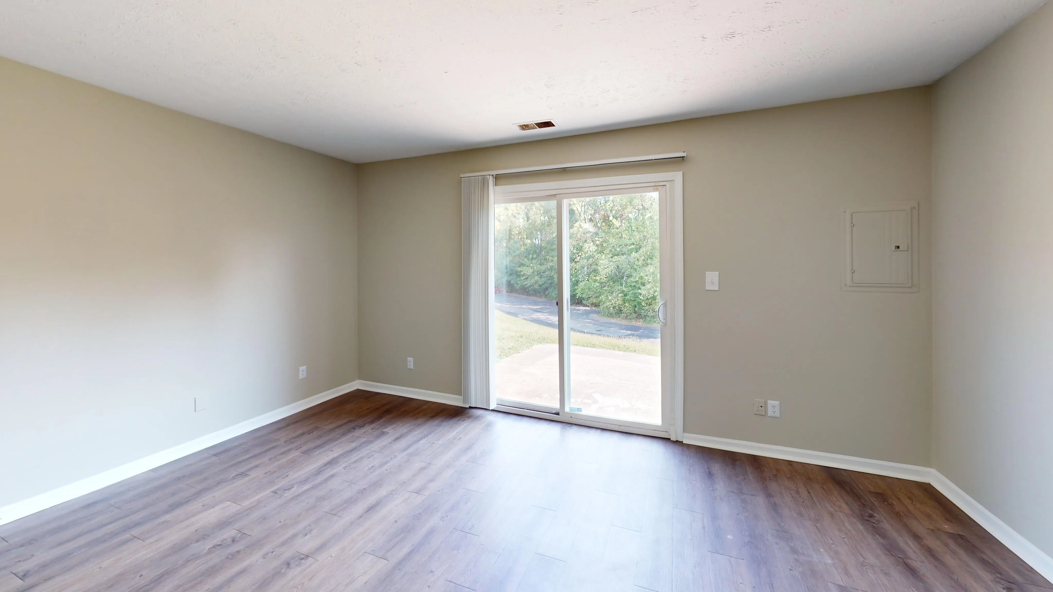 Bright living room with smooth hardwood floors and large glass sliding doors leading to a serene outdoor view.