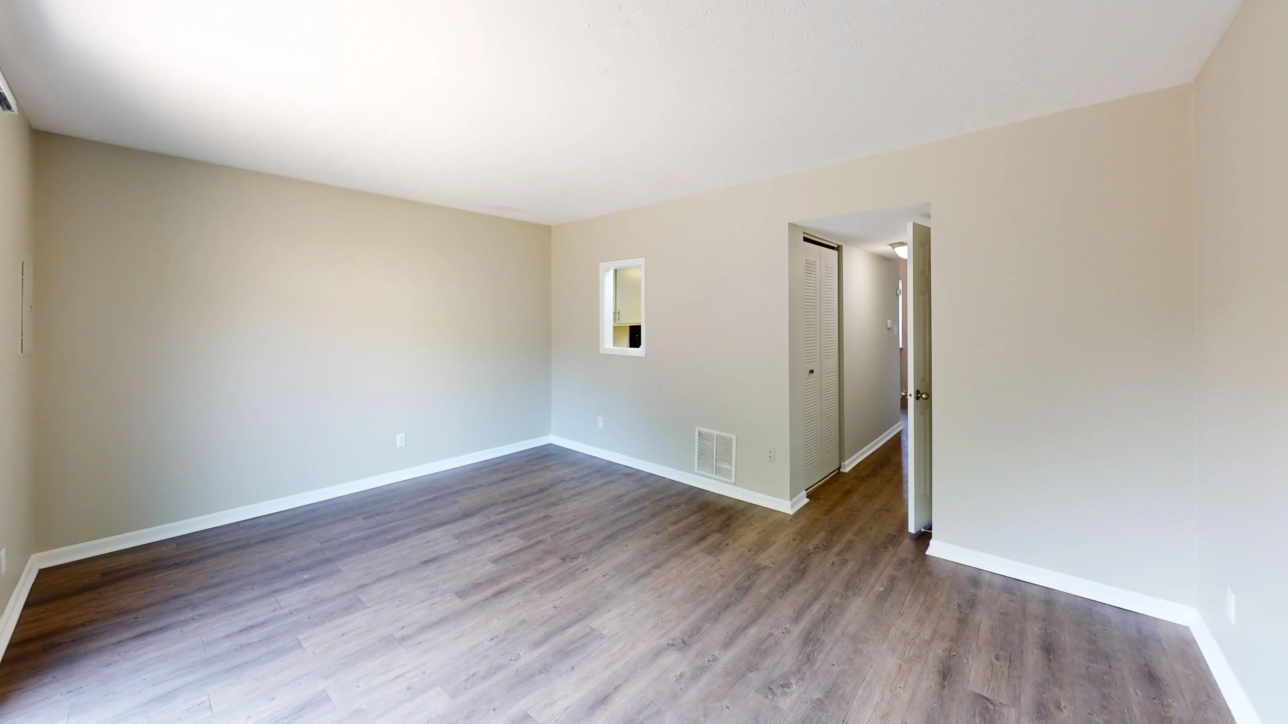 Bright and airy living room with stylish wooden flooring and neutral walls, featuring a small passthrough window and ample natural light.