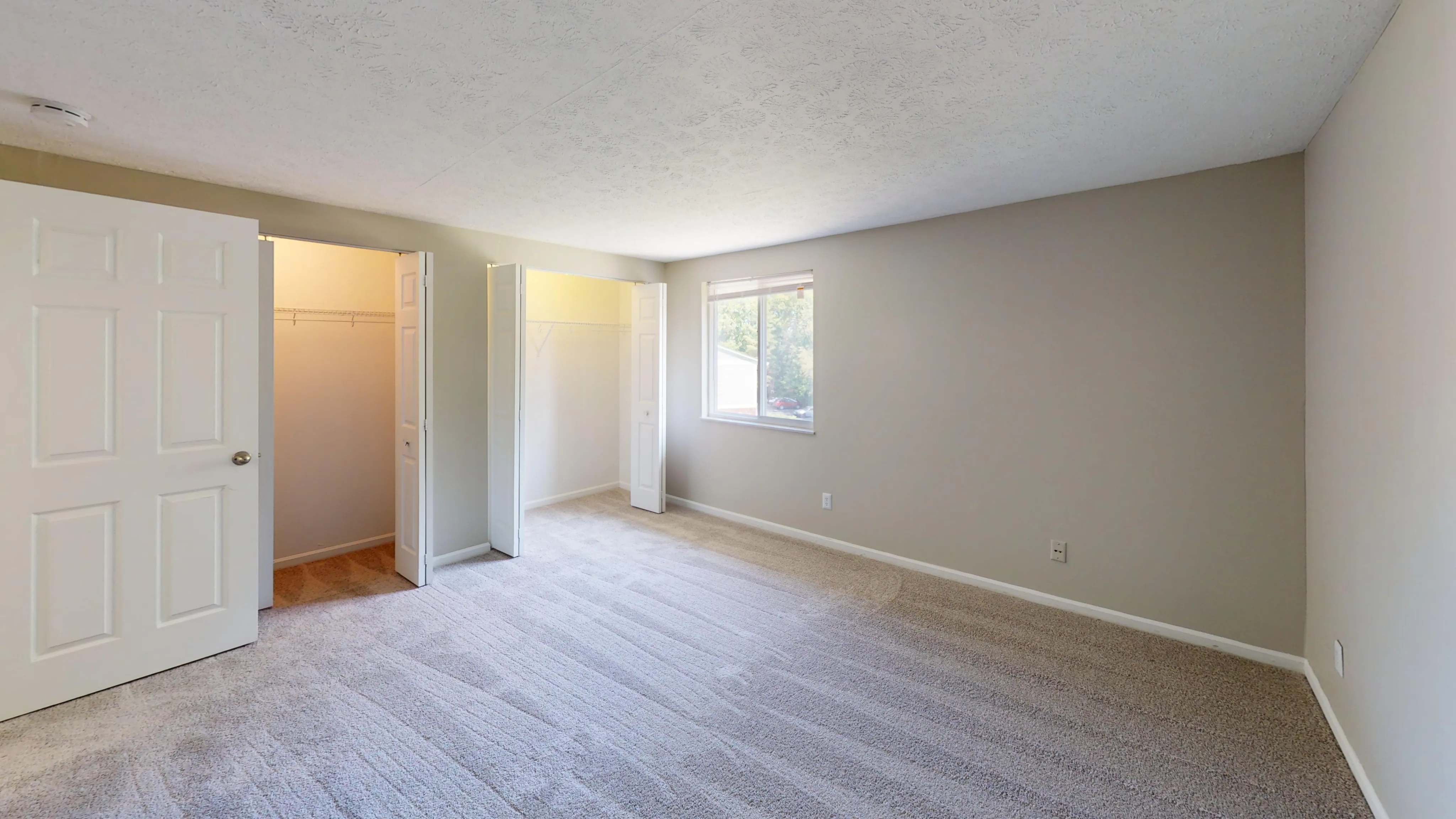 Bright and spacious bedroom with plush carpeting and a large window, featuring ample closet space and inviting neutral walls.