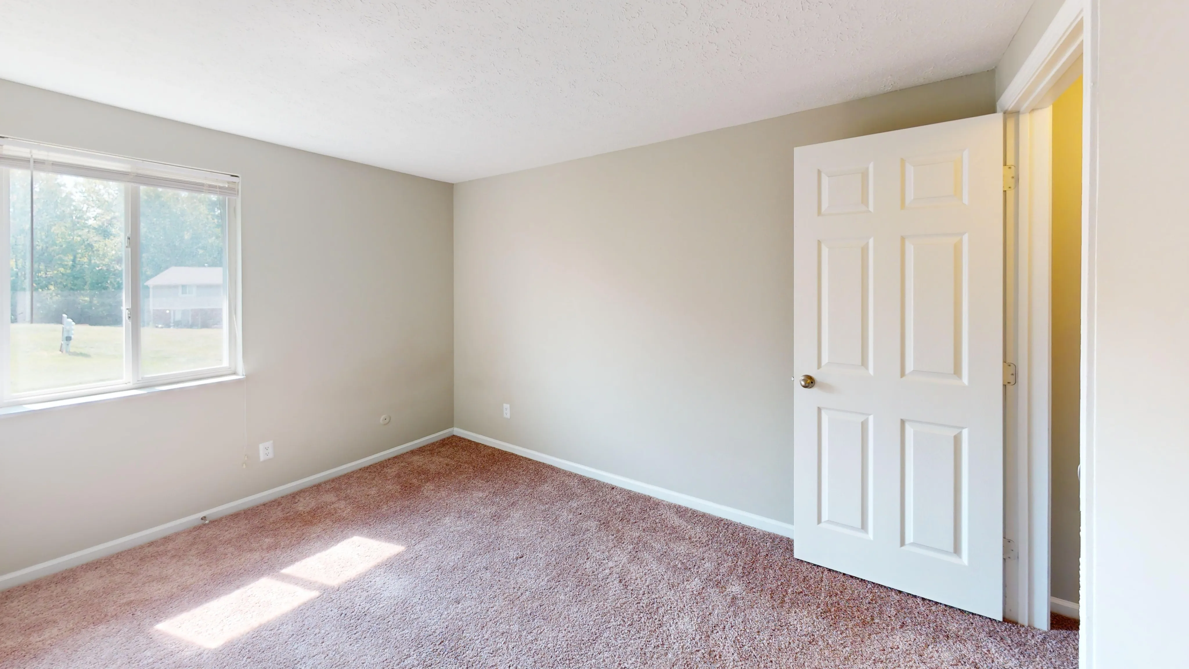 Bright, cozy bedroom with soft carpet, large window and open door, perfect for relaxation and personal comfort.