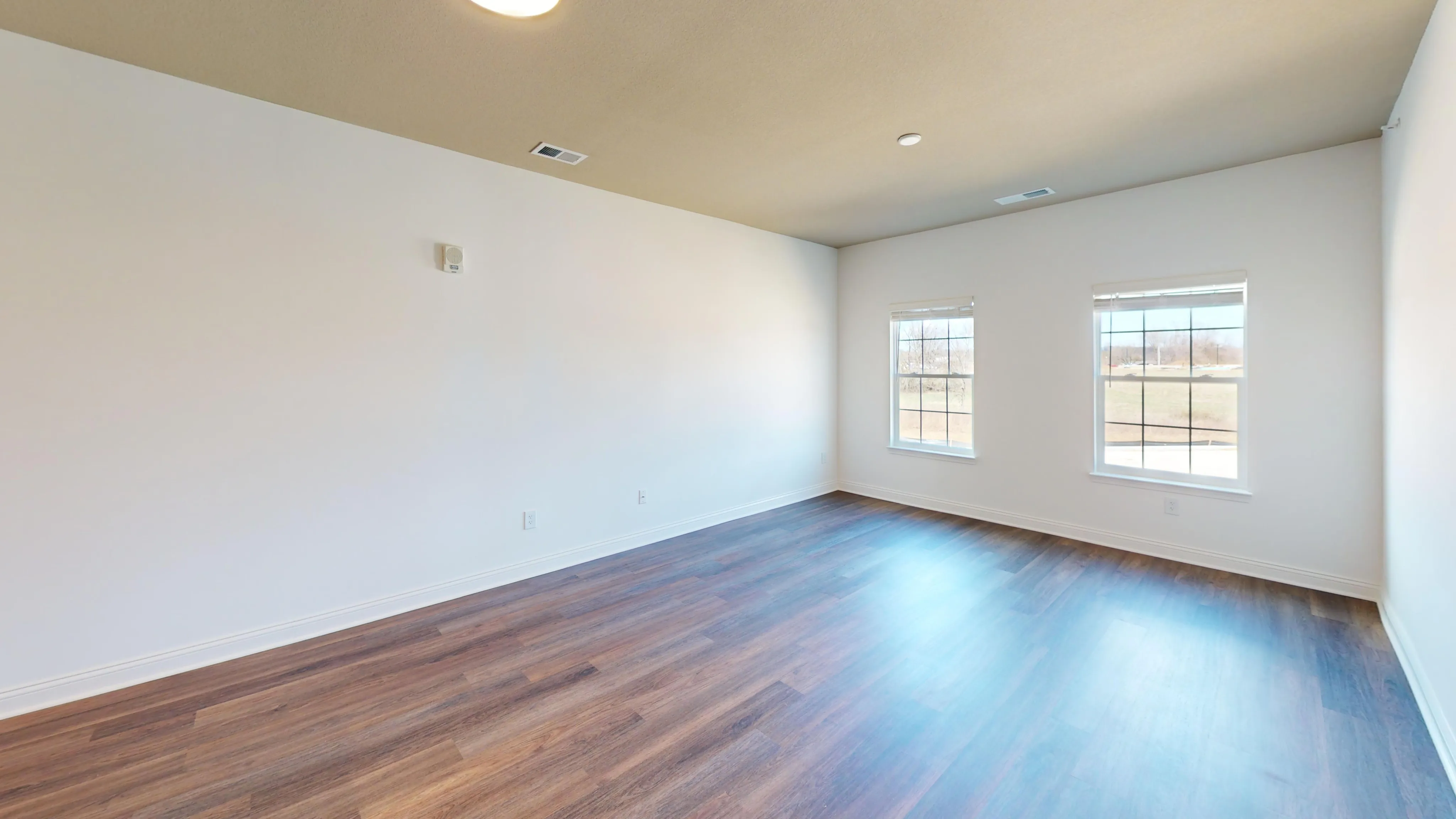 Bright living room with hardwood floors and two large windows.