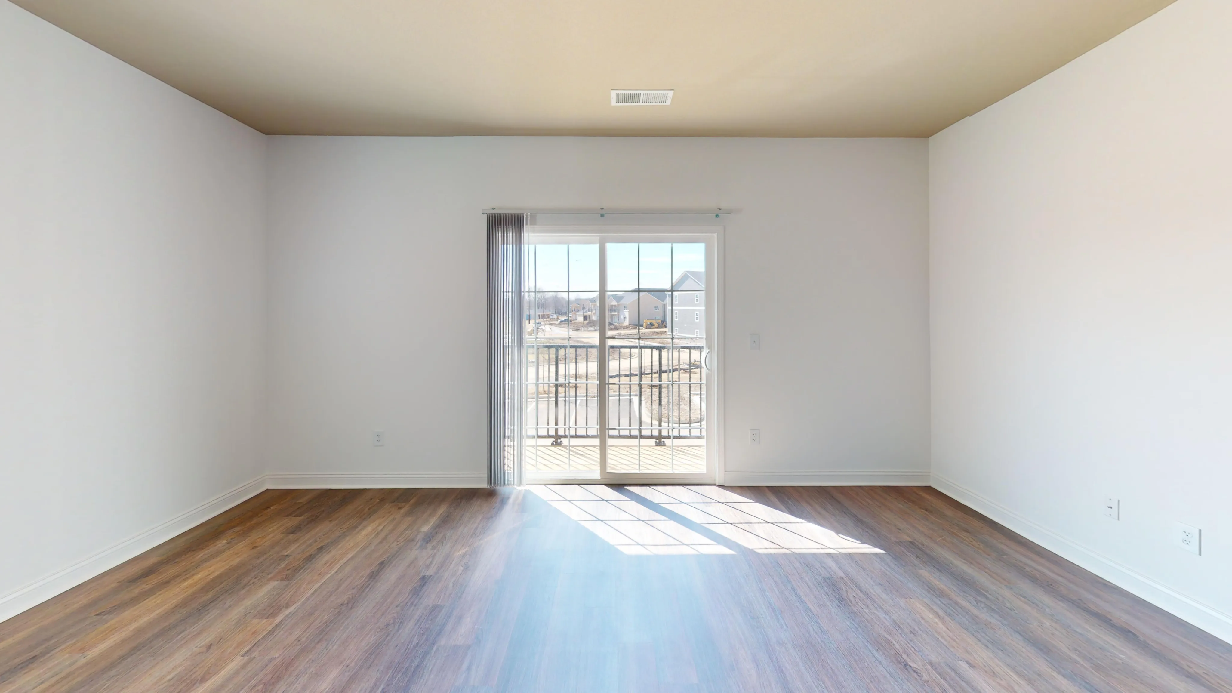 Bright and airy unfurnished living room with hardwood floors and sun shining through the sliding glass door that leads to a private balcony.