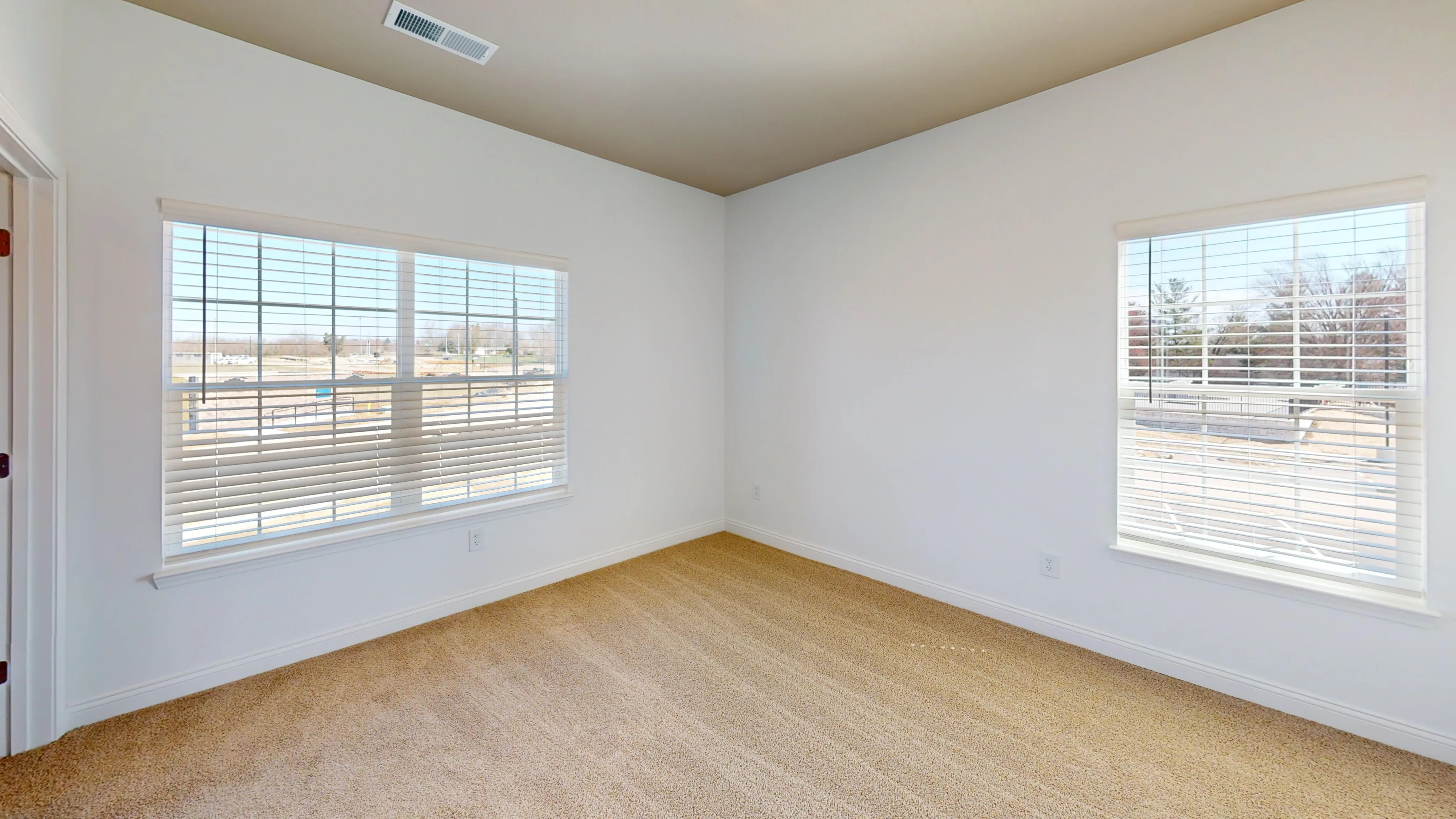 Bright and inviting room with neutral carpeting, large windows, and stylish blinds for ample natural light.