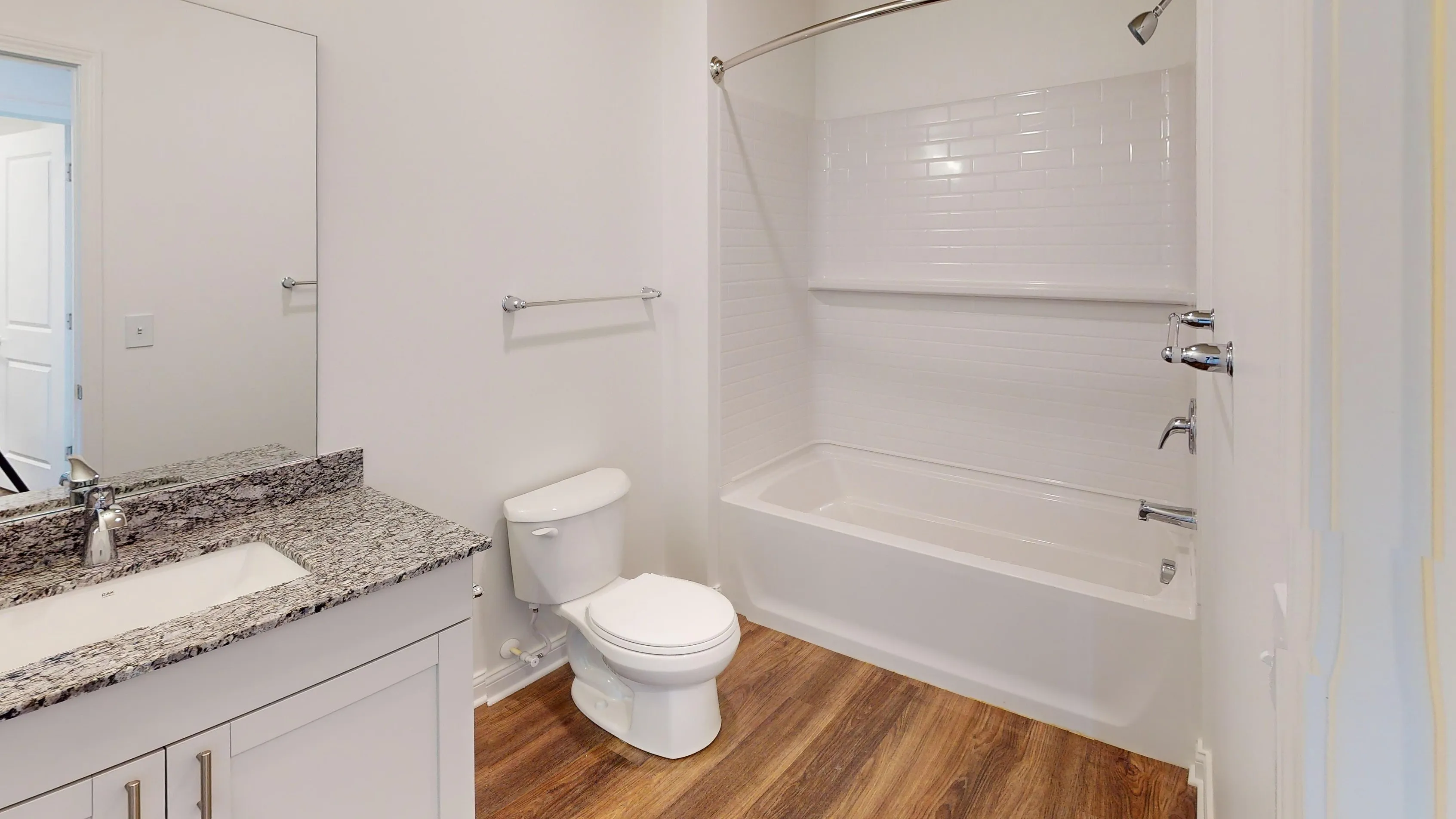 Modern bathroom with elegant granite countertop, sleek white vanity, and inviting wood flooring.