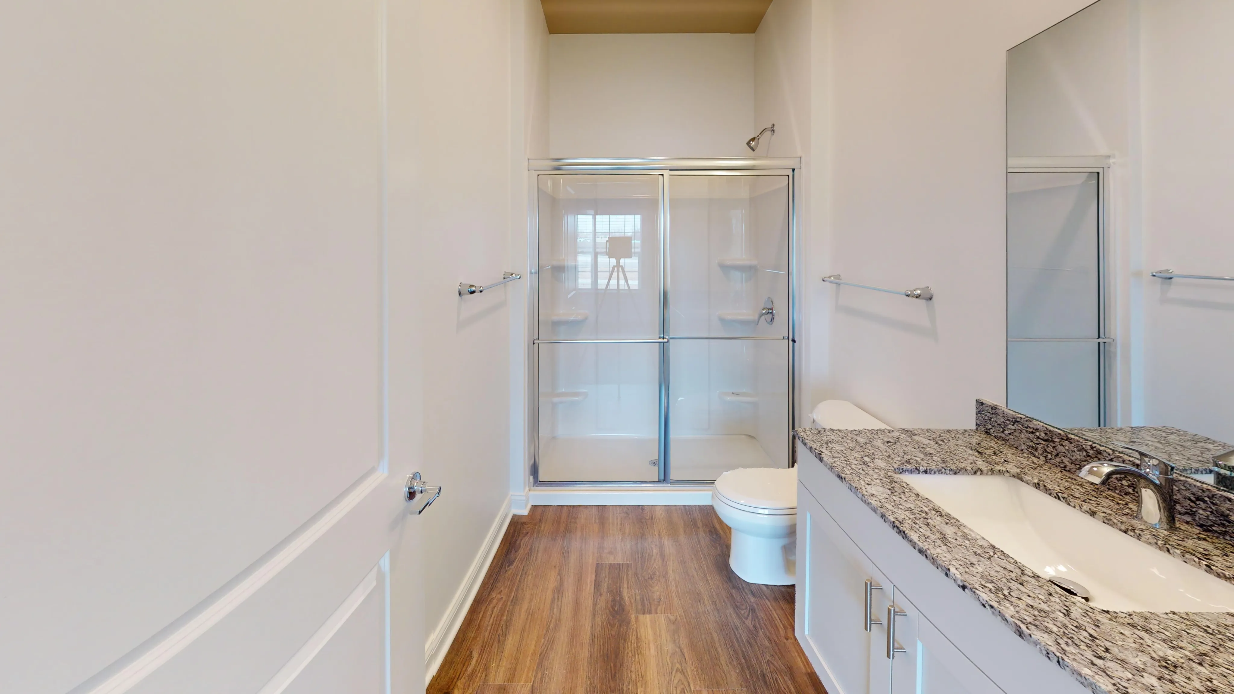 Elegant bathroom featuring a sleek glass shower, granite countertop, and polished wood flooring.