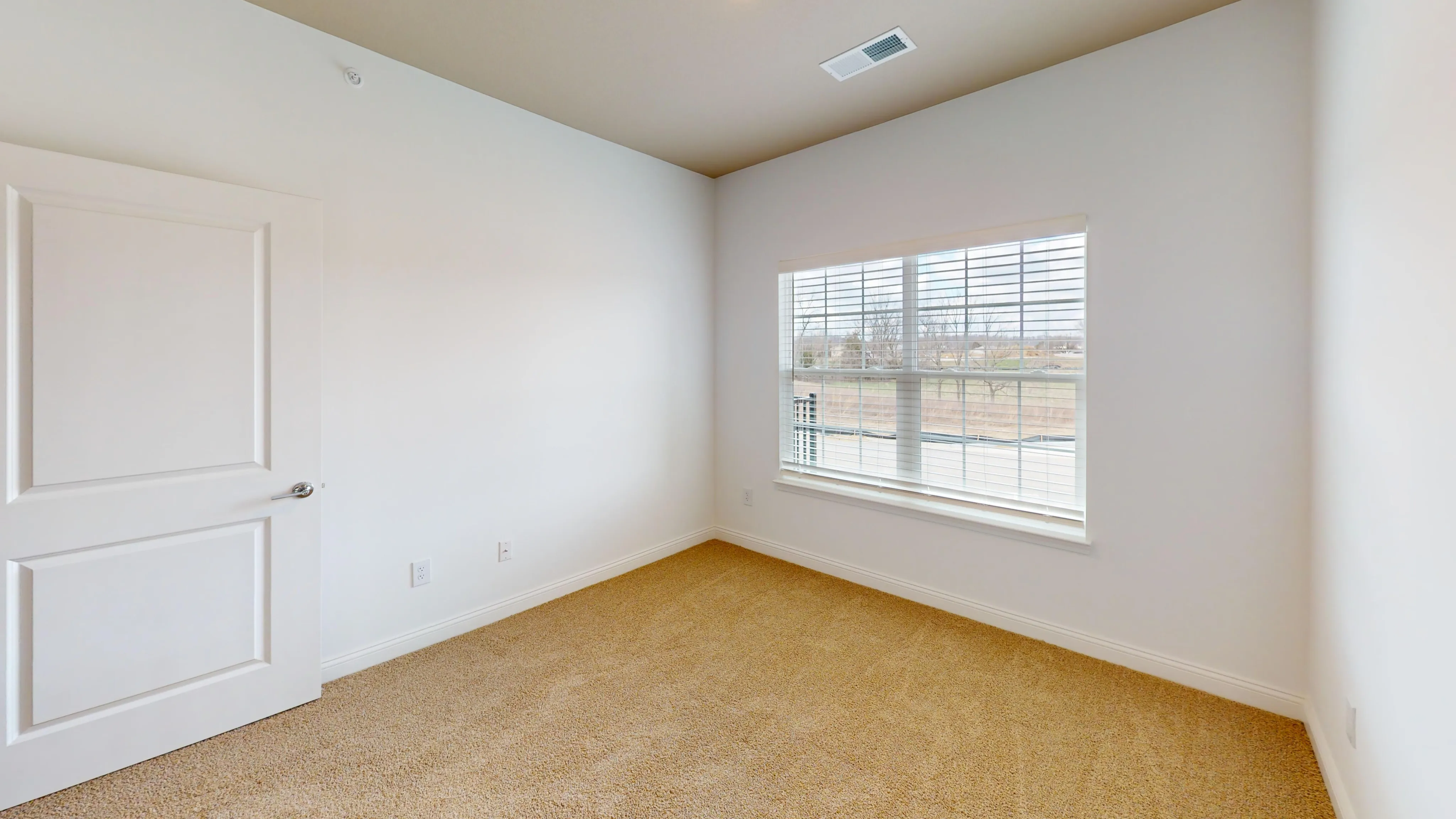 Cozy apartment bedroom with plush carpet and a large window offering lots of natural light.