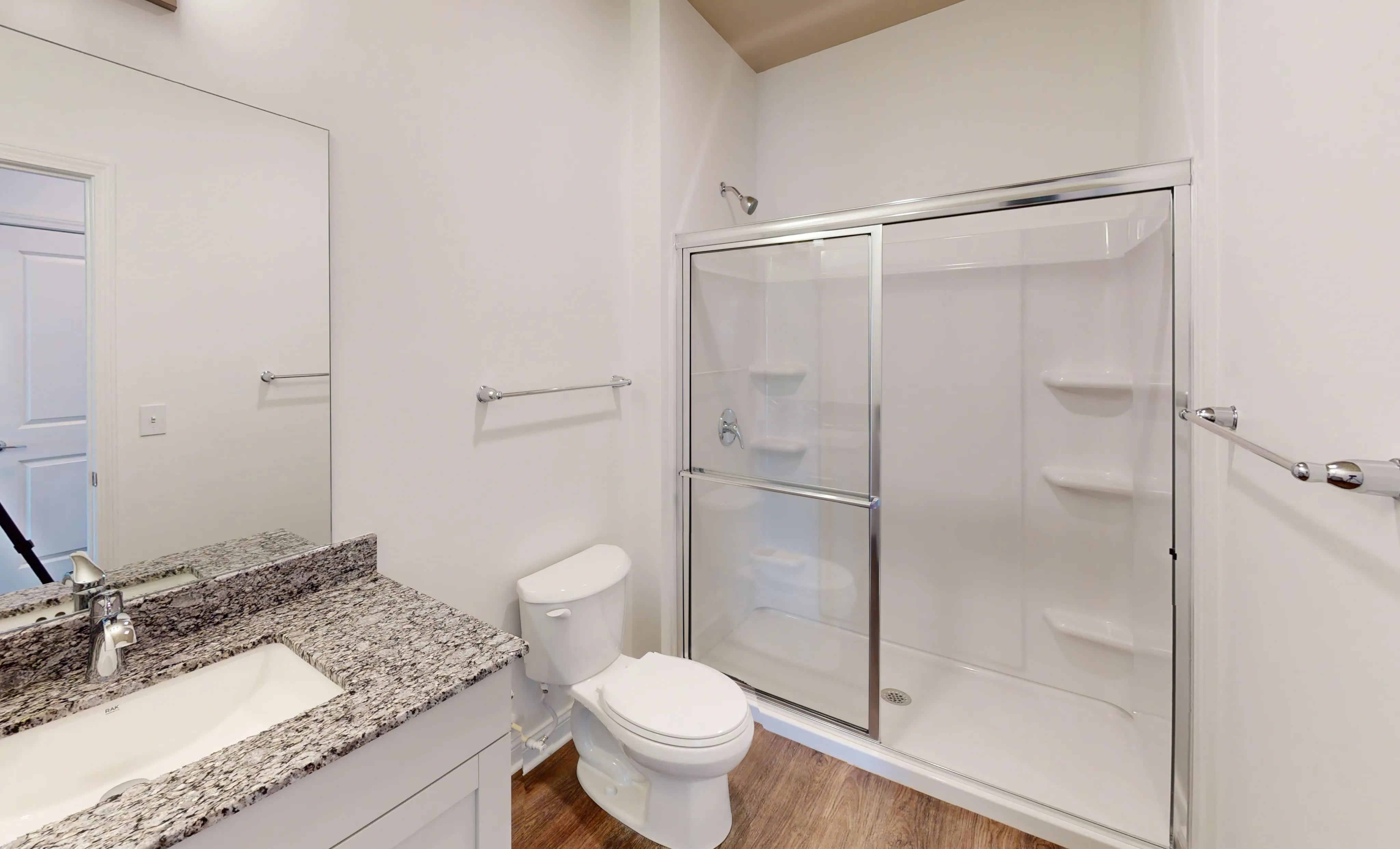 Modern bathroom featuring sleek granite countertops, a spacious glass-enclosed shower, and elegant wood flooring.