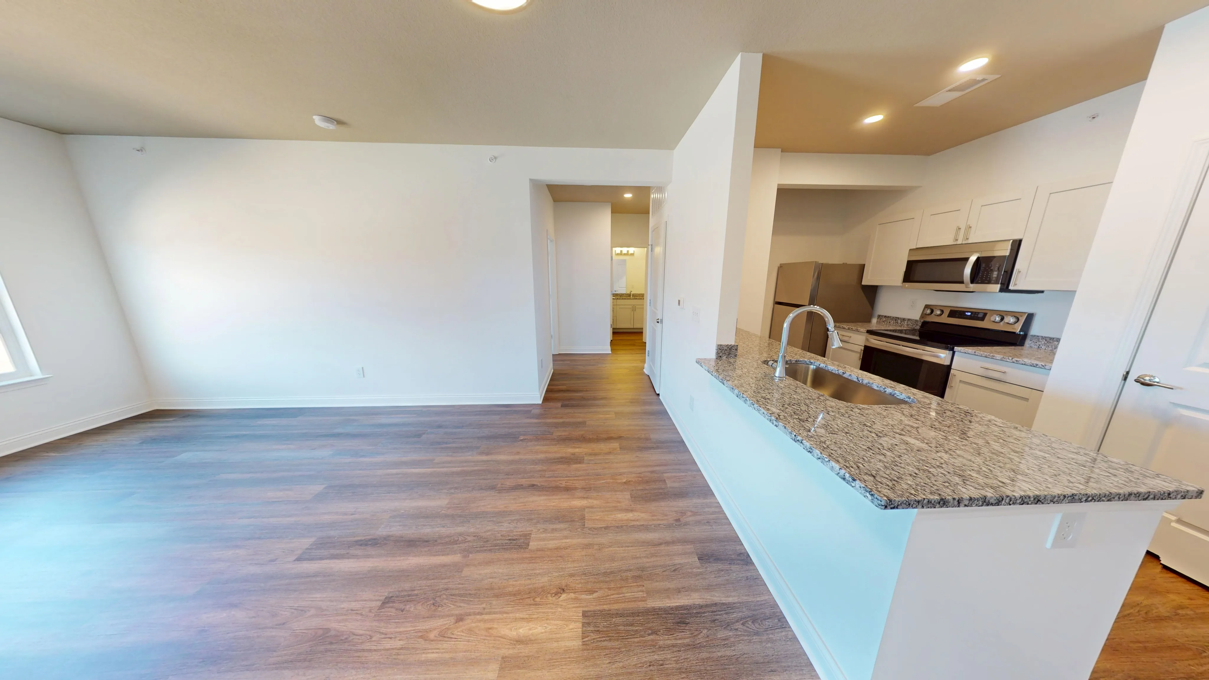 Modern open-concept kitchen with sleek granite countertops, stainless steel appliances, and elegant hardwood flooring extending into a bright living area.