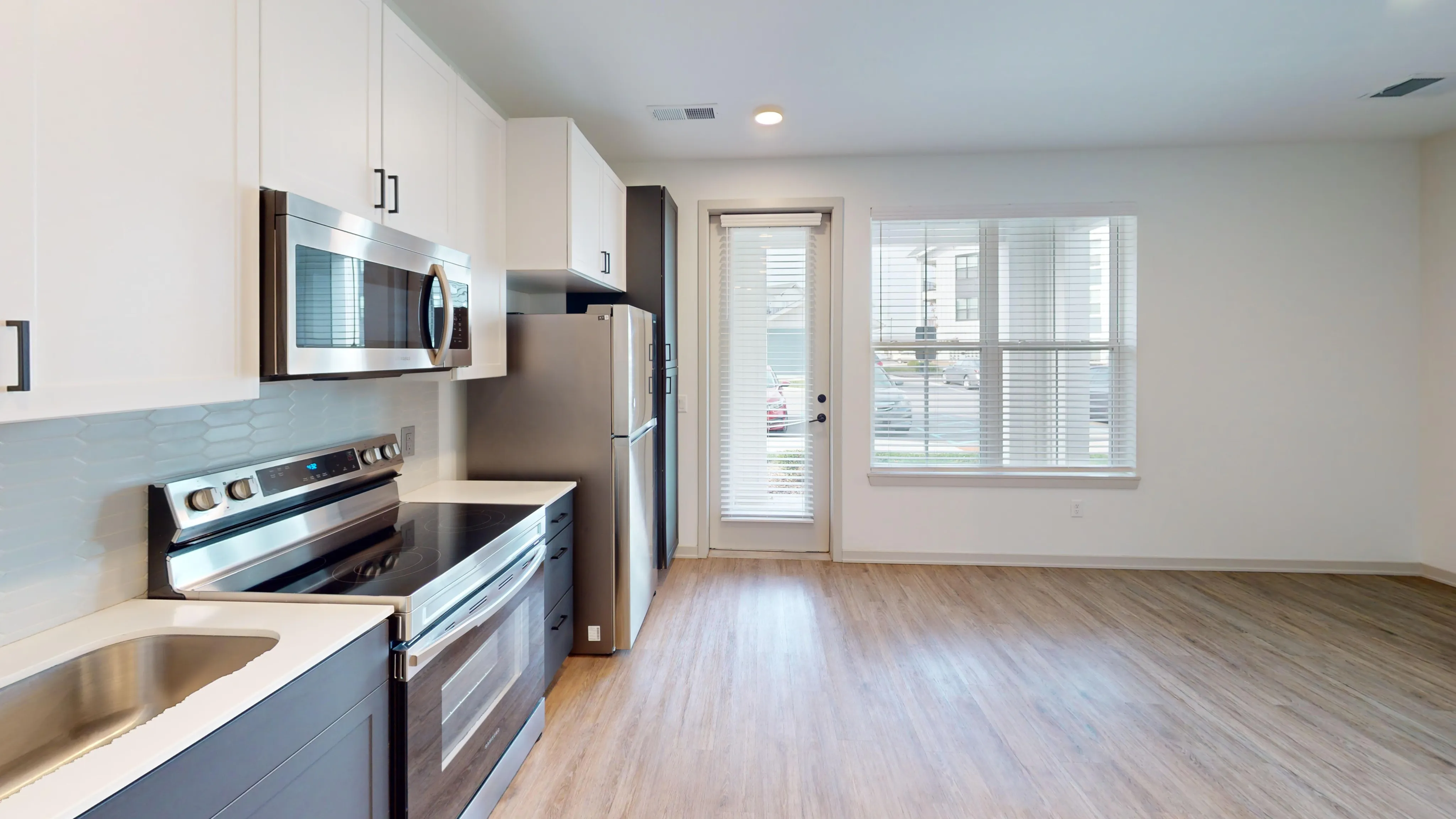 Modern kitchen with sleek stainless steel appliances, inviting wood flooring, and abundant natural light from large windows.