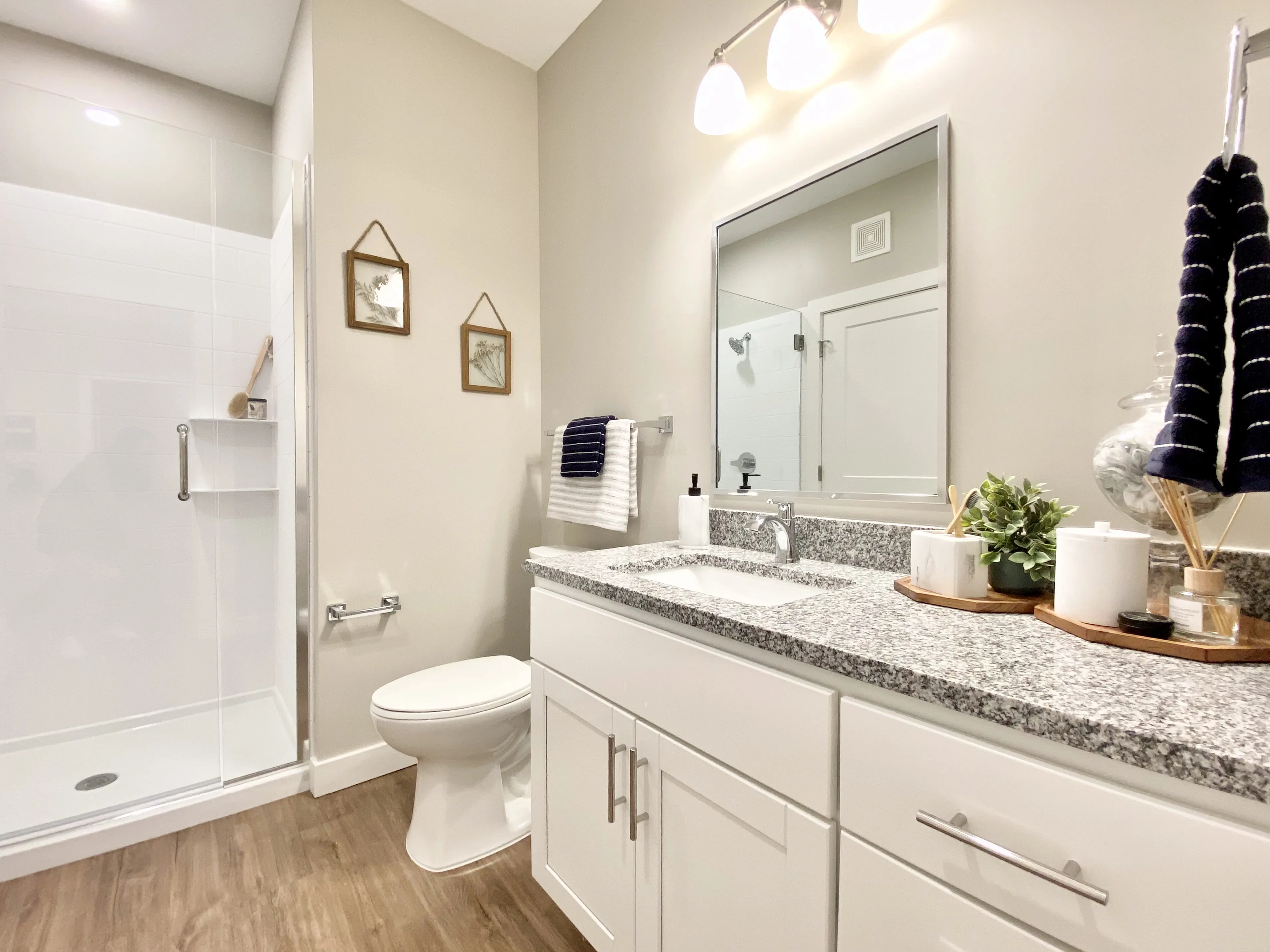 Bright and modern bathroom featuring sleek granite countertops, elegant lighting, stylish decor, and a spacious glass-enclosed shower.