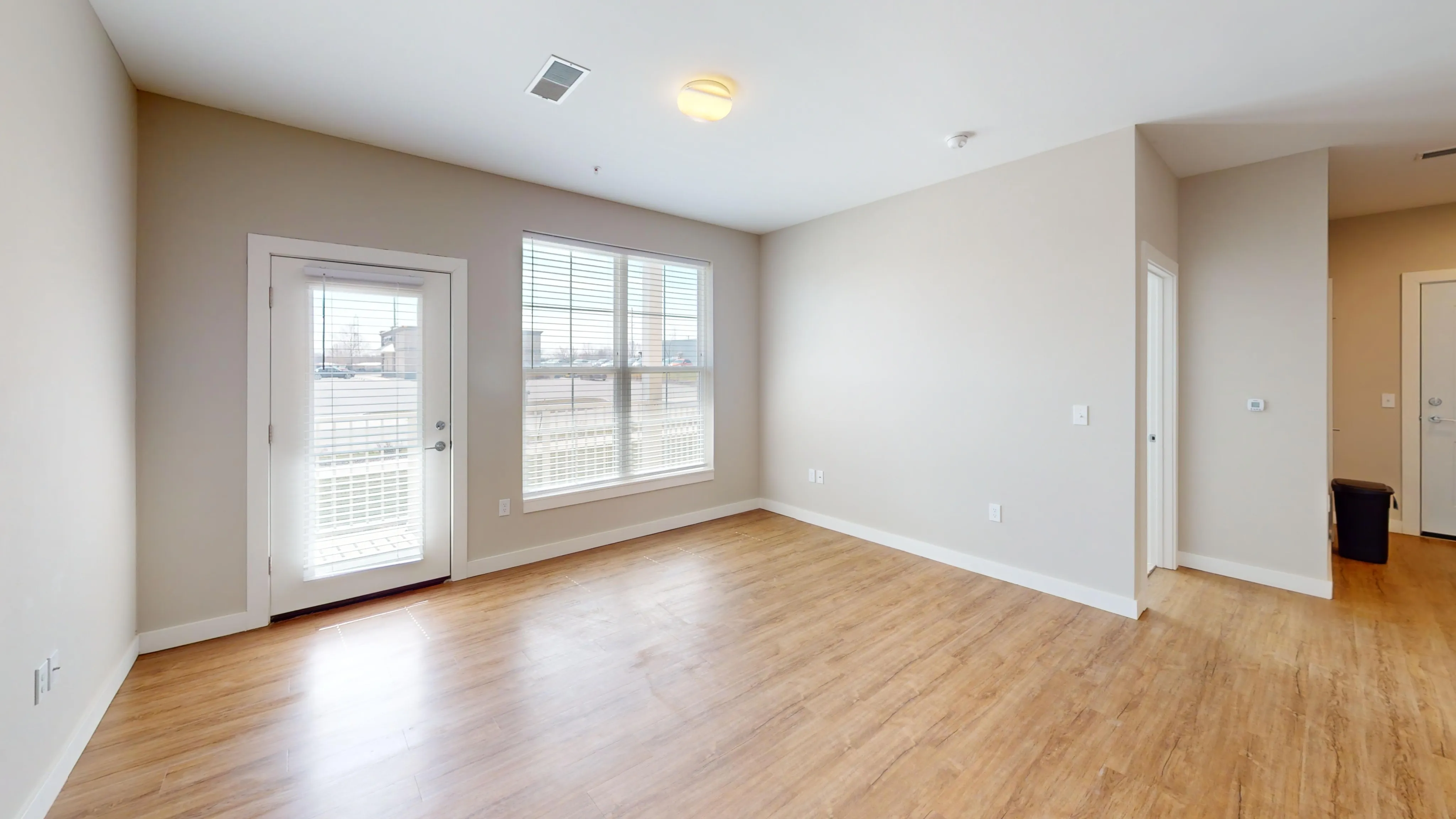 Bright, modern room with hardwood floors, large windows for natural light, and a glass door opening to a balcony.