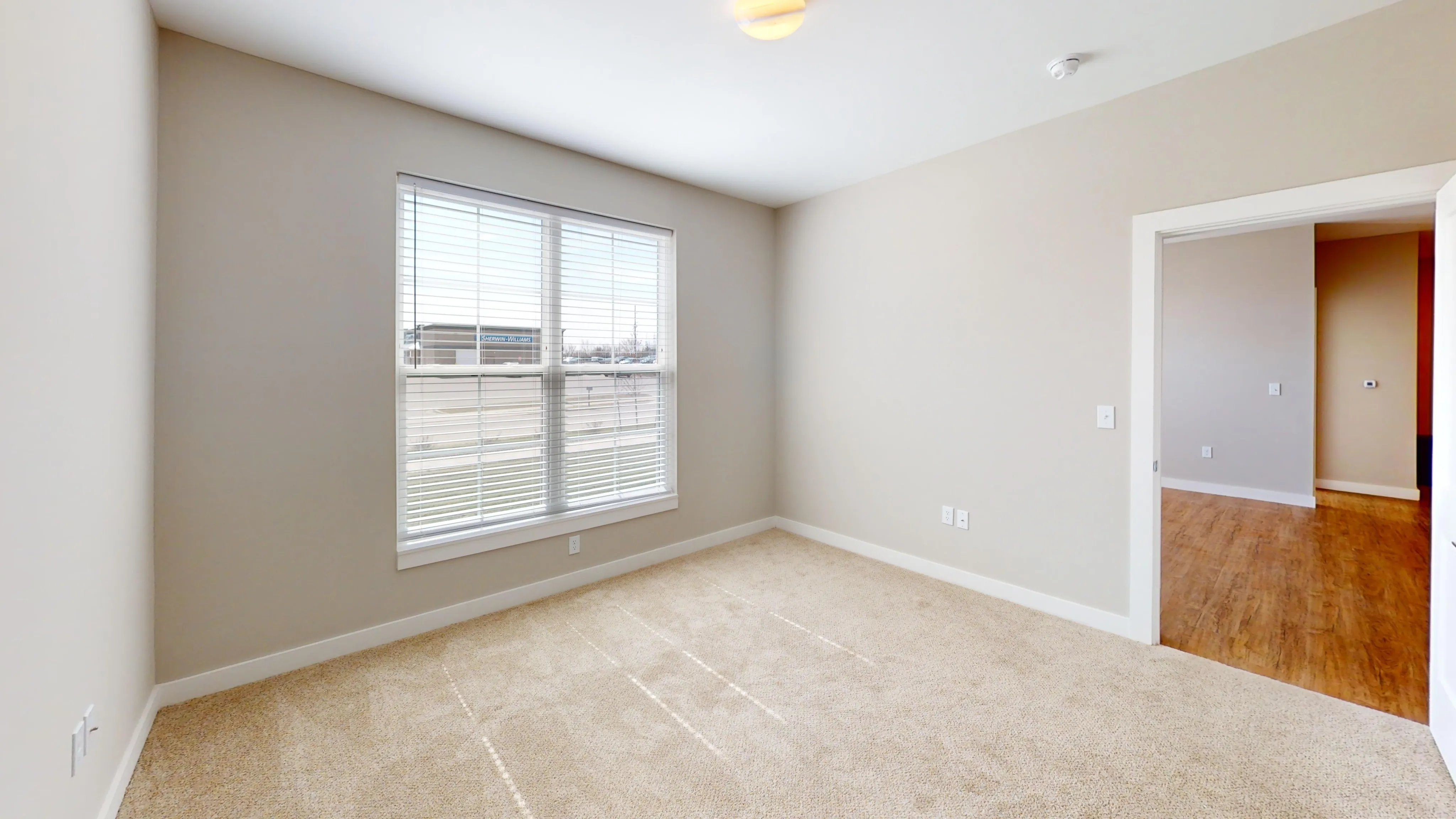 Bright and airy bedroom with large window and plush carpet flooring, offering a warm and inviting atmosphere.