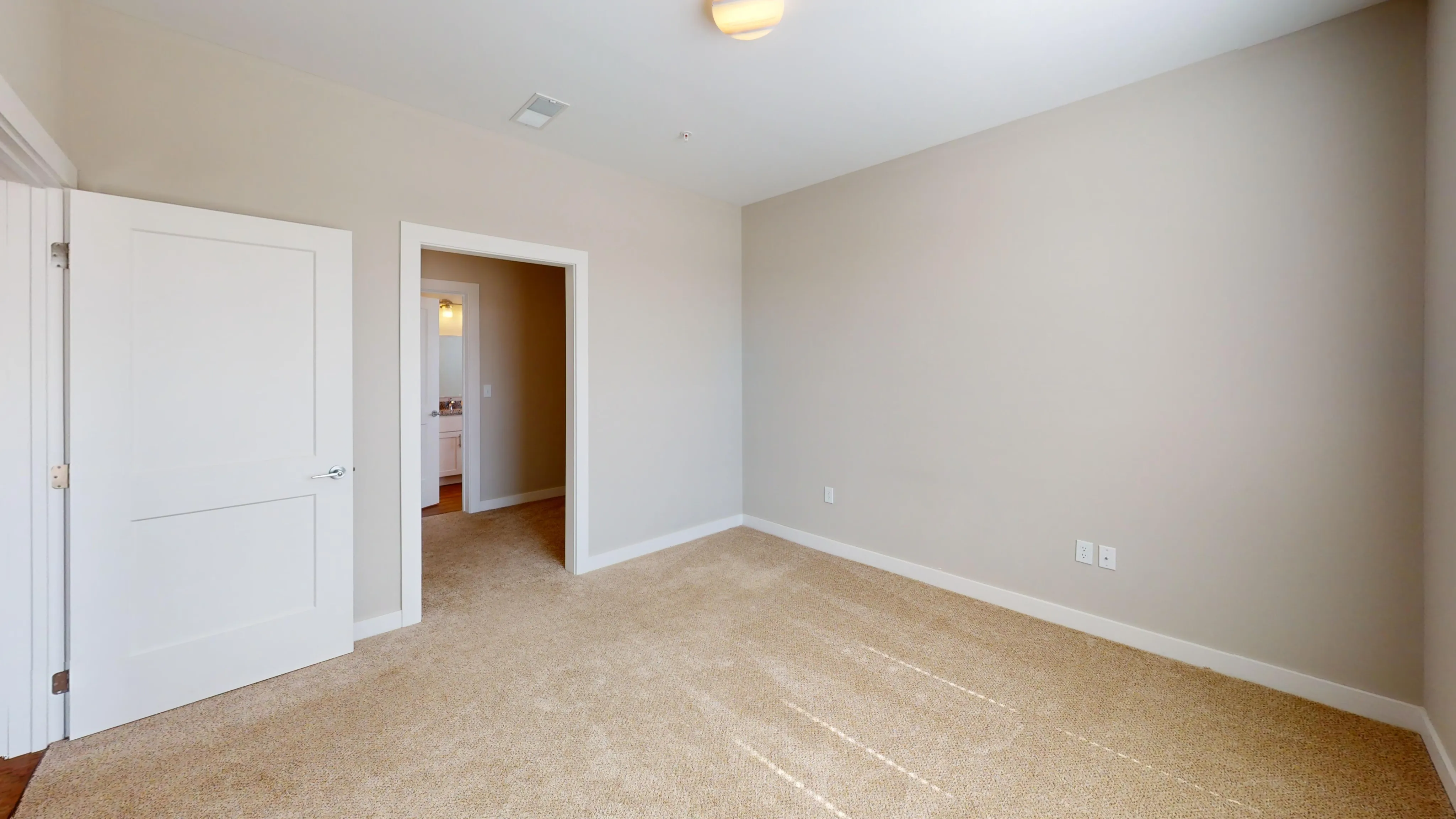 Bright and spacious room with fresh neutral walls and plush carpet, adjacent to a well-lit bathroom, ideal for personalization.