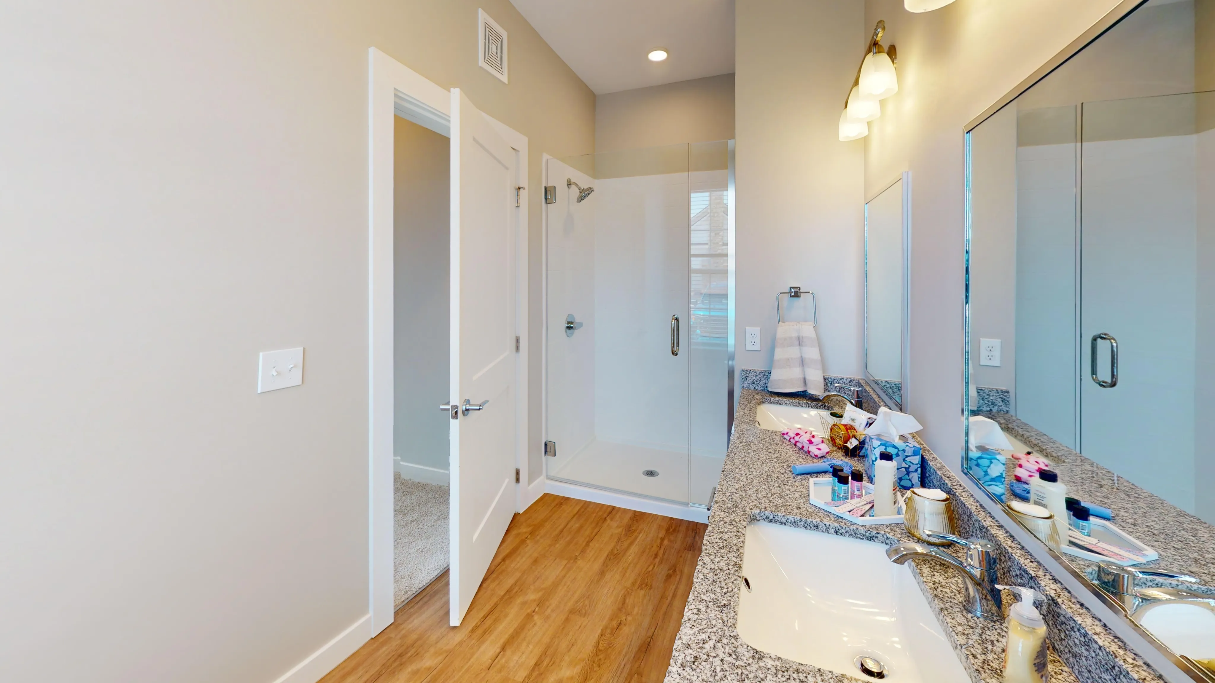 Modern bathroom featuring dual sinks with granite countertops, glass-enclosed shower, and elegant lighting.