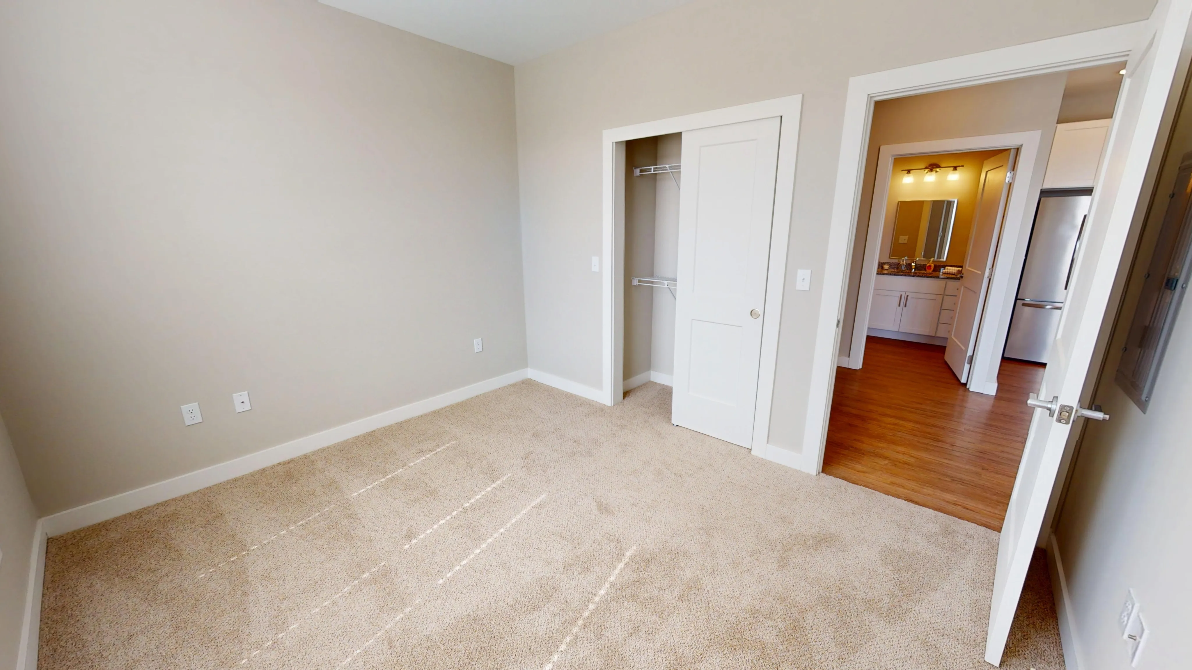 Bright bedroom with plush carpet, spacious closet, and view into modern bathroom and kitchen area.