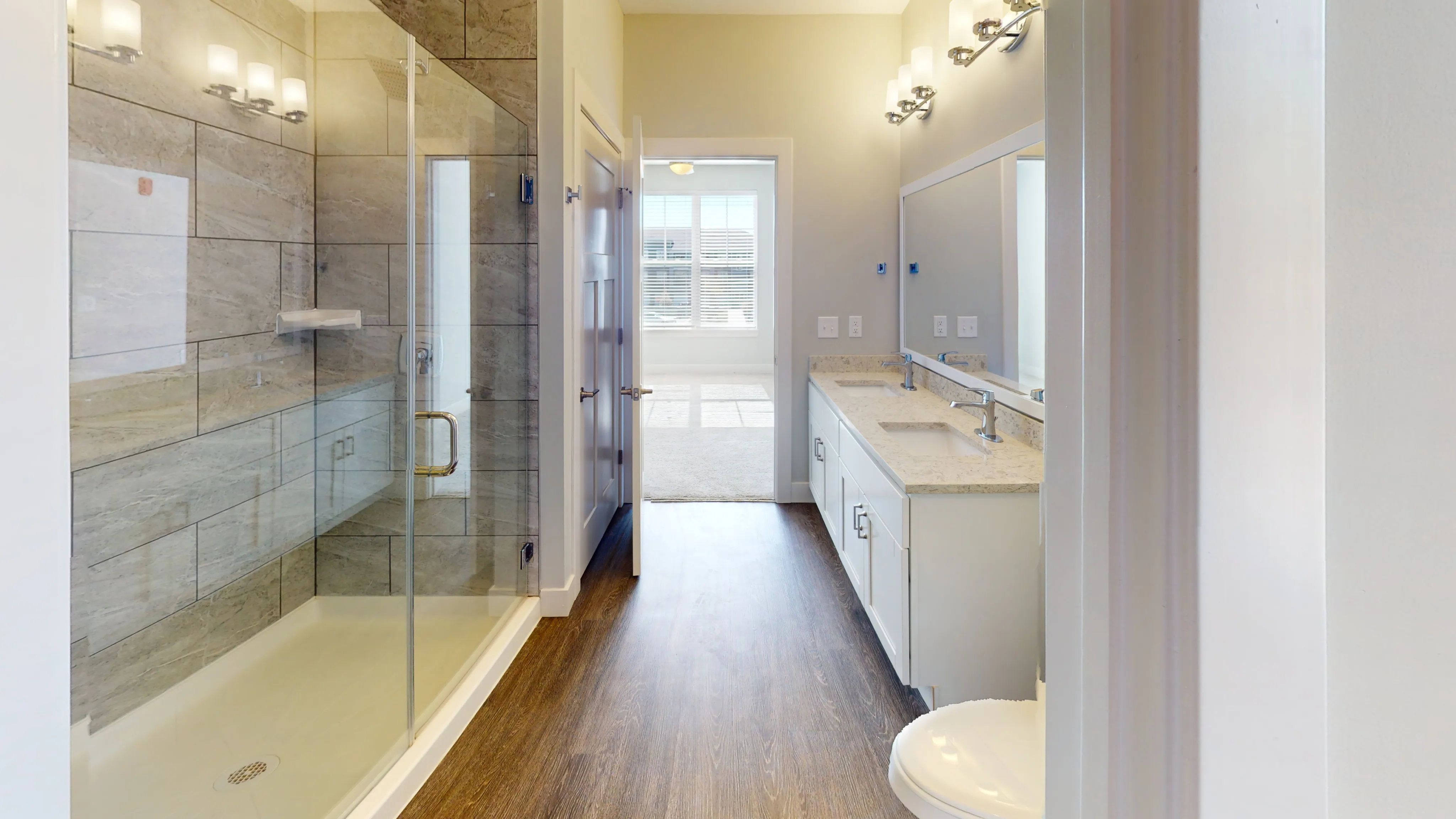 A spacious bathroom in The Redbud apartment, featuring a modern walk-in shower, dual vanity, and ample counter space.