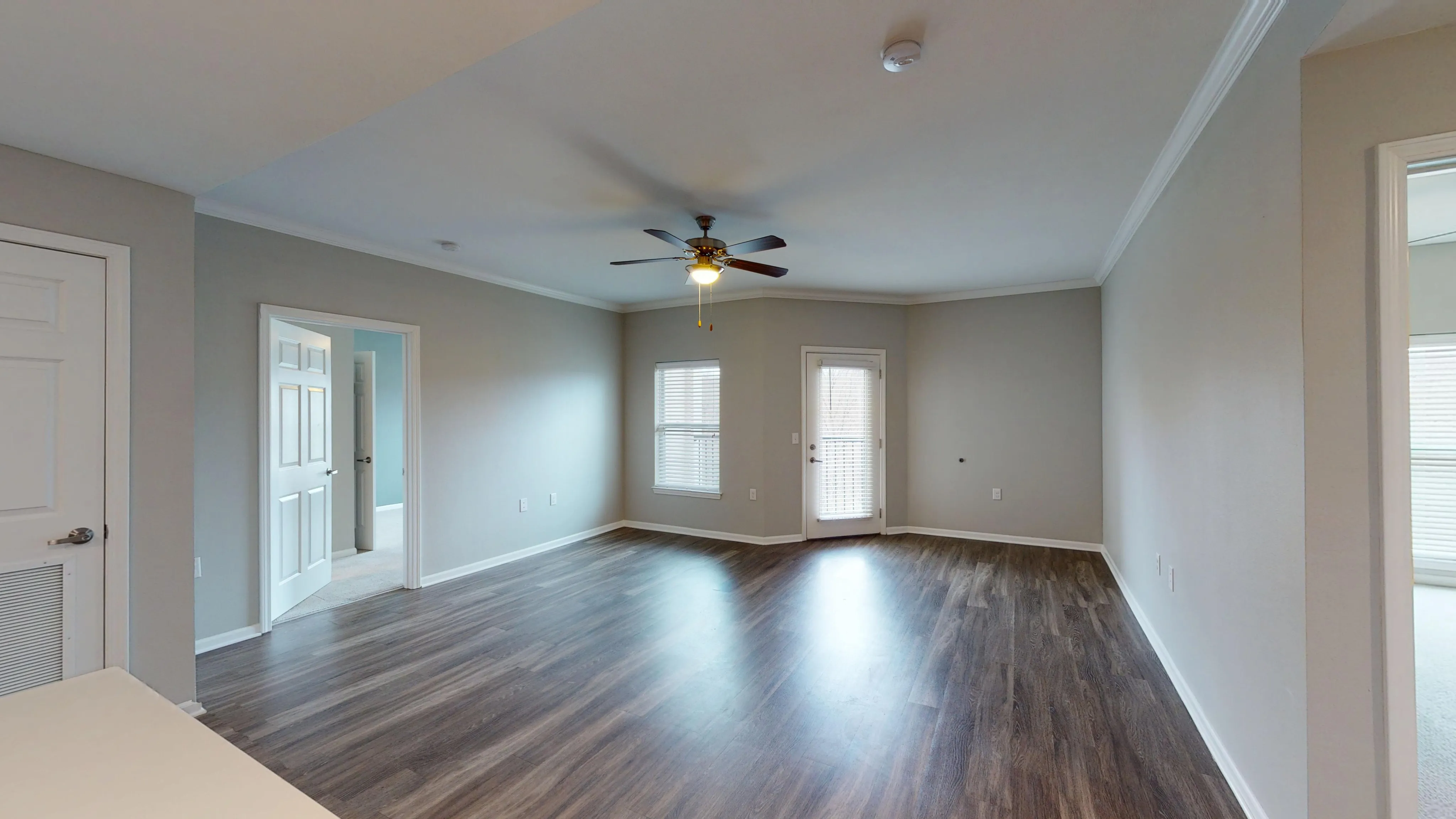 Spacious living room with elegant wooden flooring, ceiling fan, and abundant natural light.