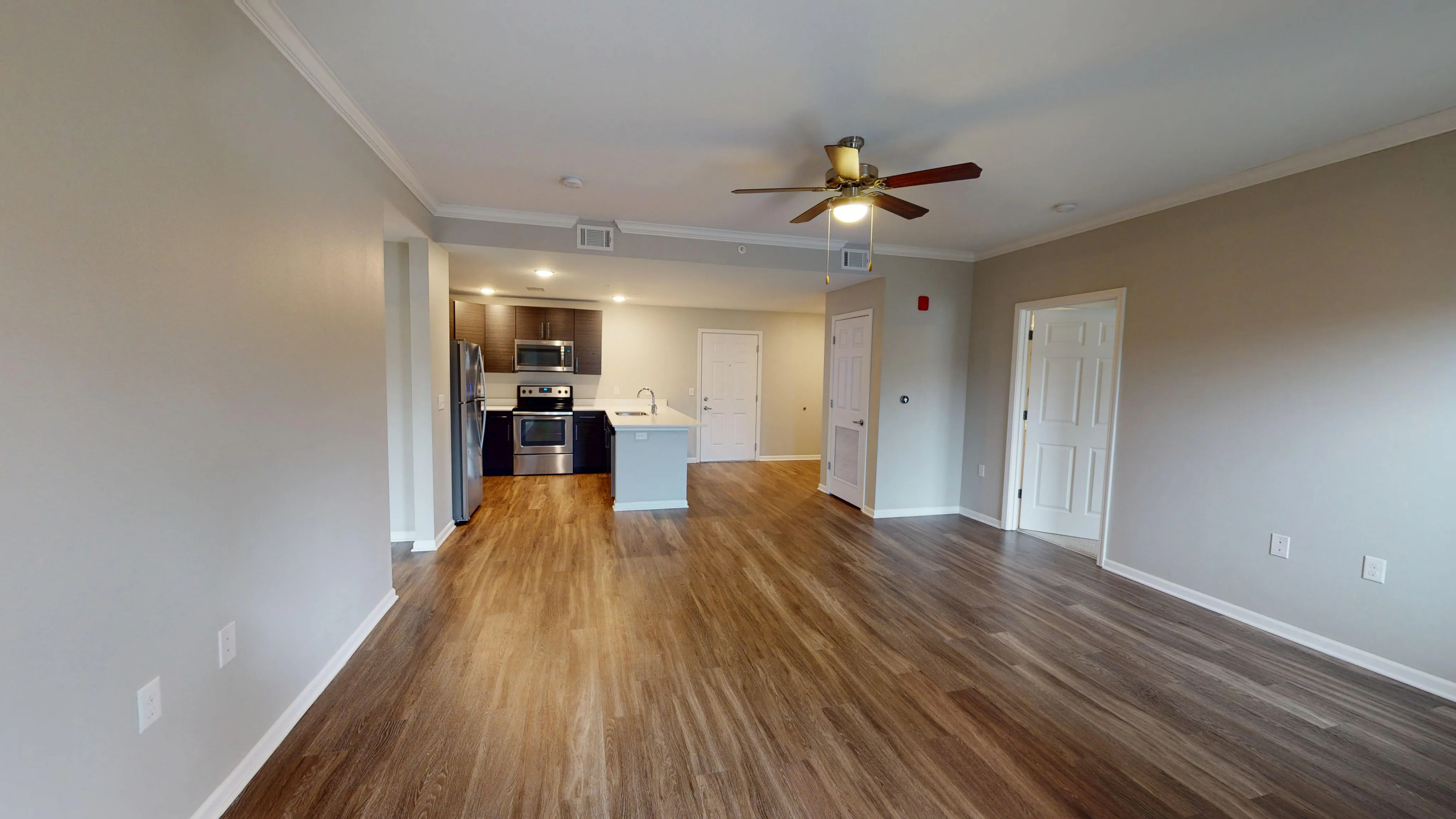 Modern open-plan apartment with elegant wood flooring, sleek kitchen with stainless steel appliances, and a ceiling fan for comfort.