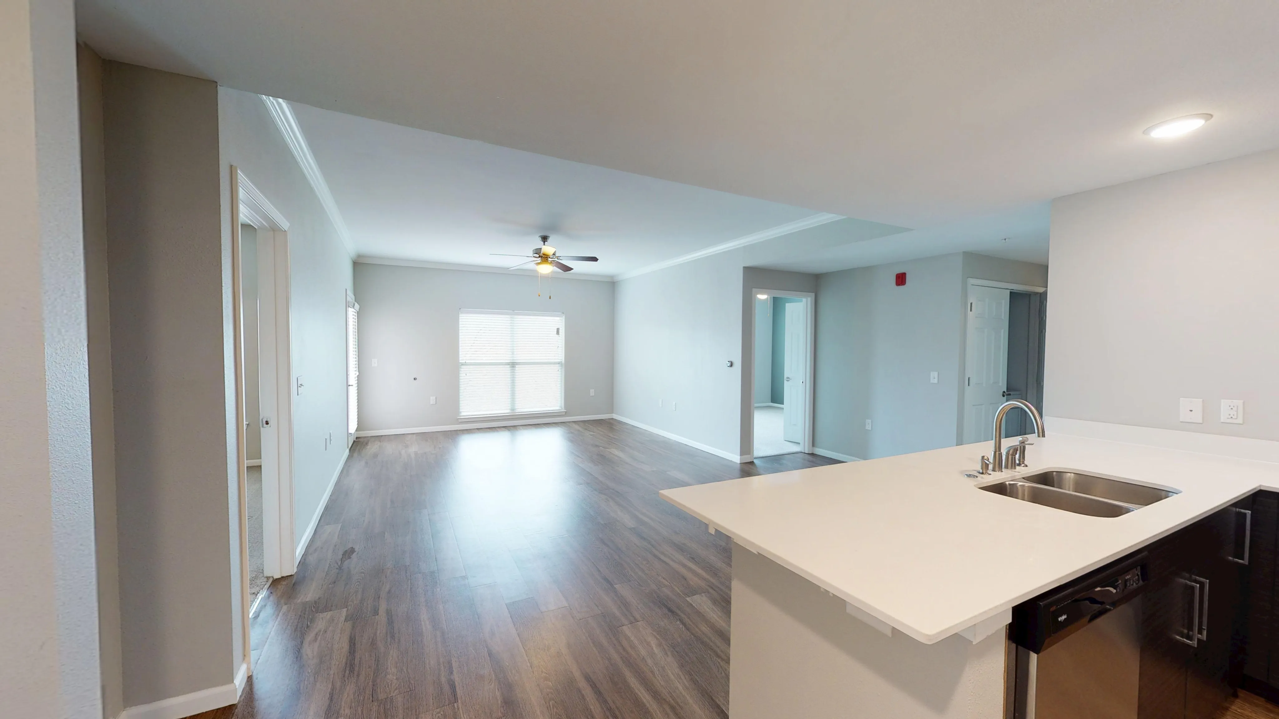 Chic open-concept living area with modern kitchen and elegant wood flooring, featuring ample natural light and a ceiling fan.