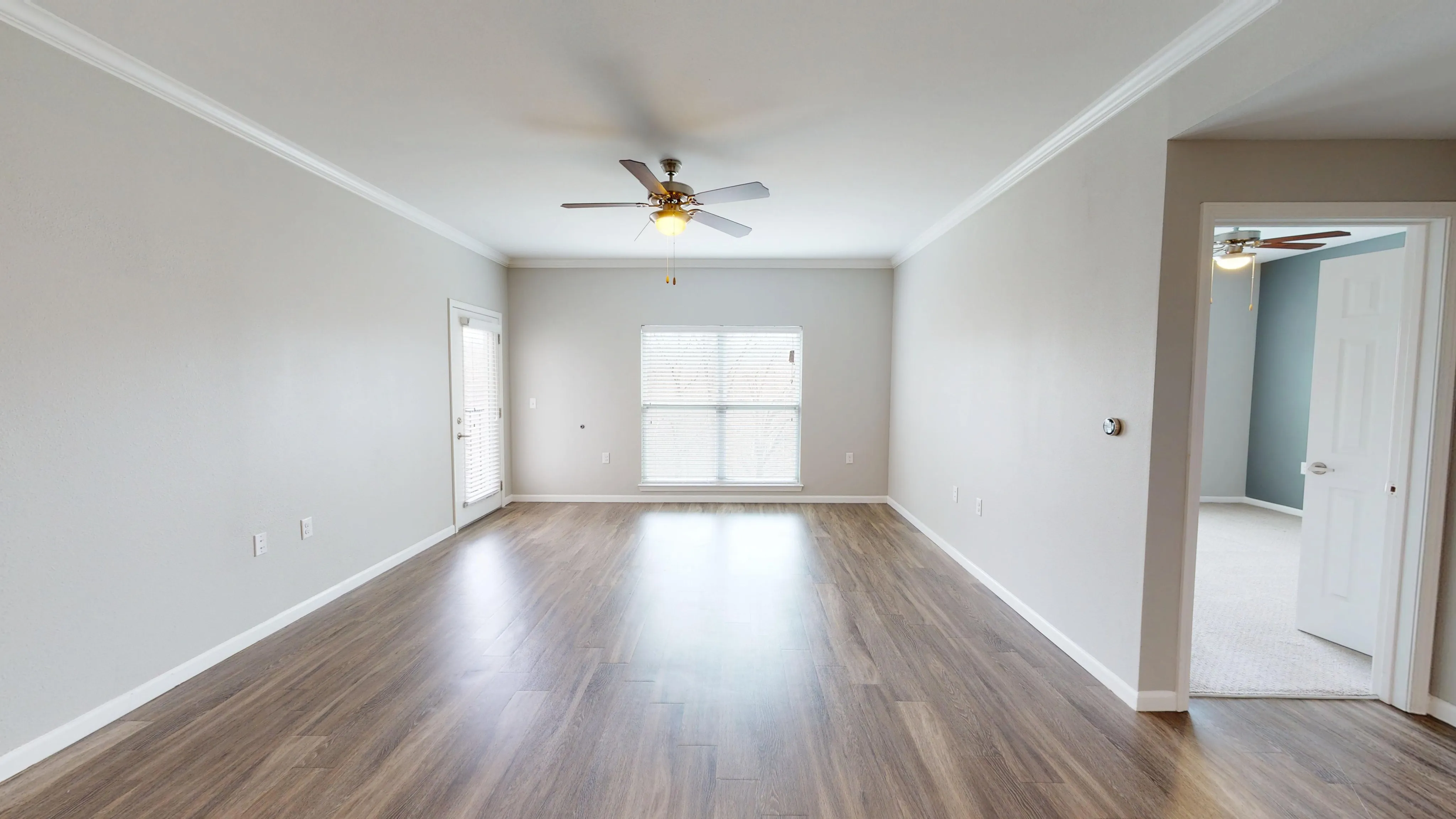Bright and spacious living room with elegant wood flooring, modern ceiling fan, and inviting natural light through large windows.