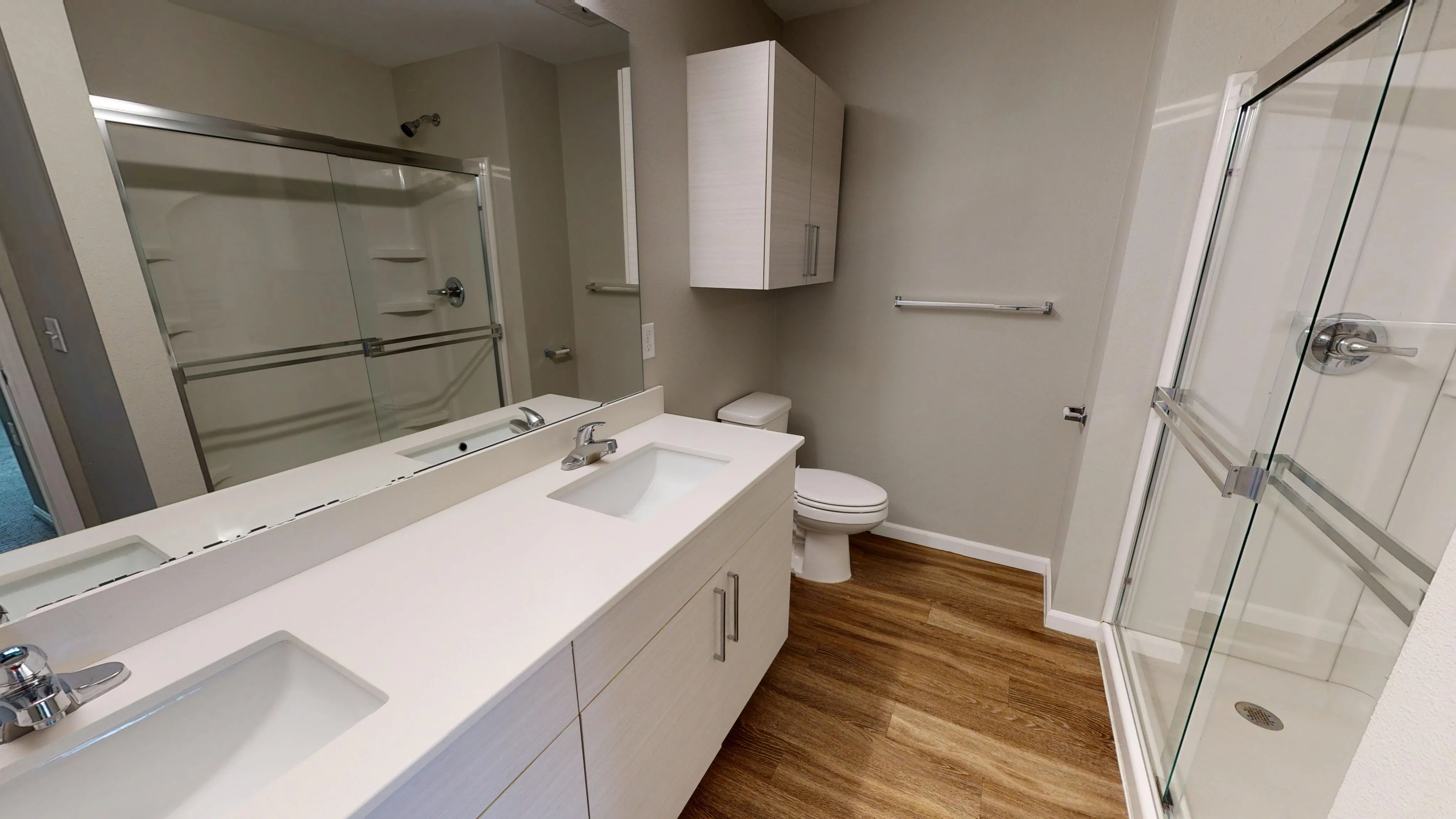 Elegant modern bathroom with a sleek glass shower, double sink vanity, and wood-style flooring.