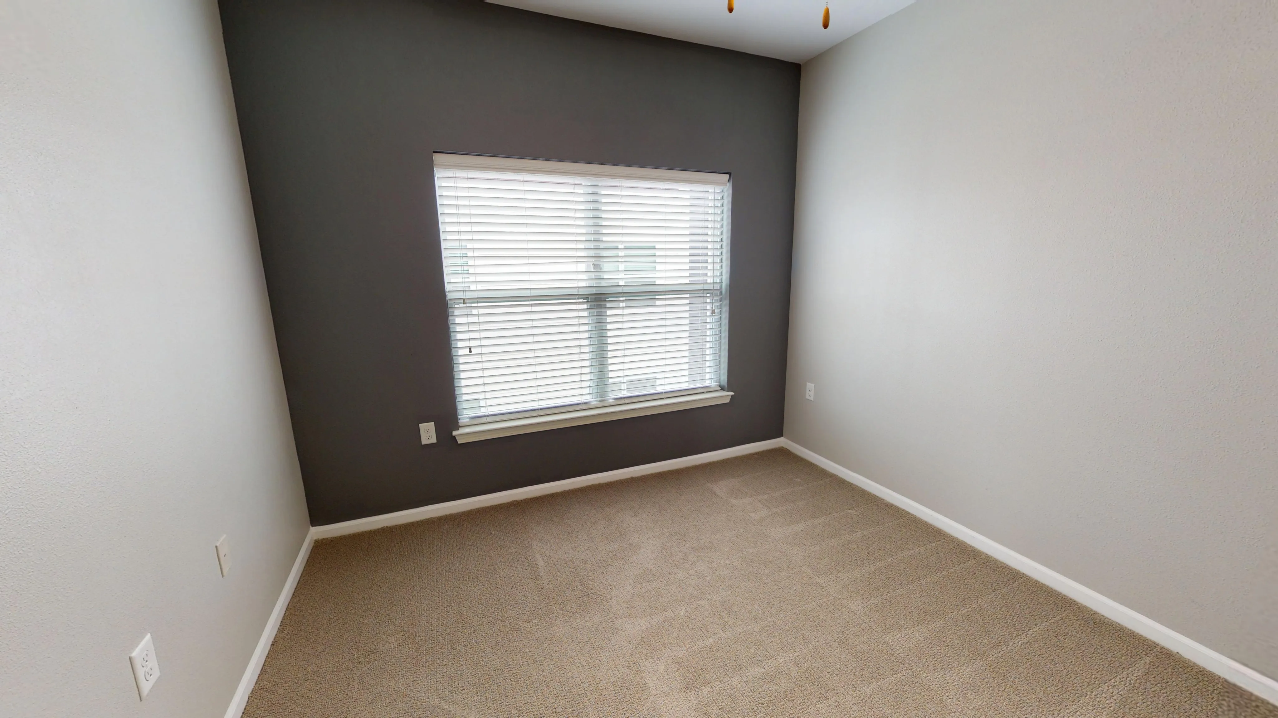 Bright, cozy room featuring soft carpeting, neutral walls, and a large window with blinds.