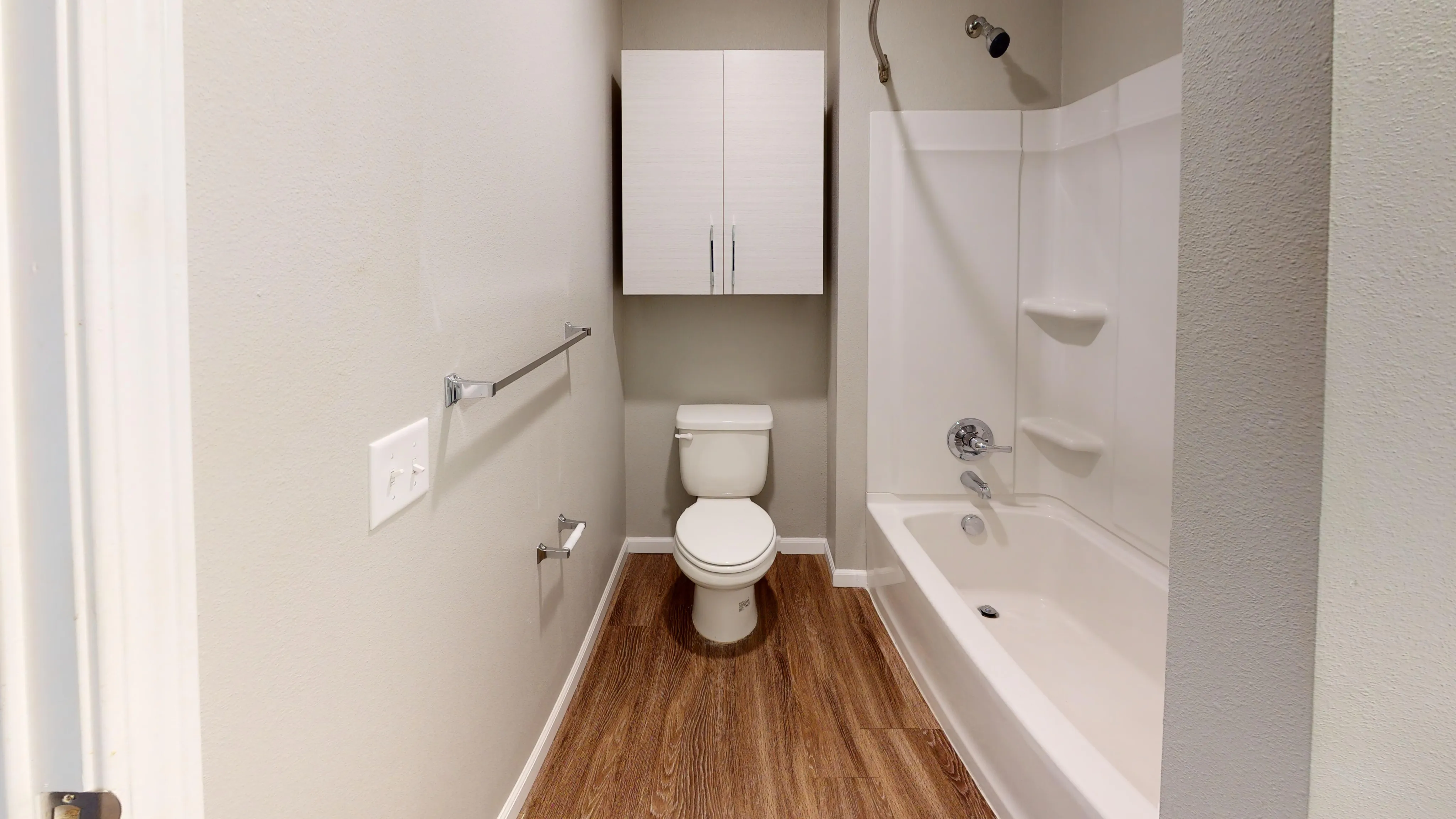 Elegant bathroom with modern fixtures, featuring a sleek vanity cabinet, pristine white bathtub, and wood-style flooring.