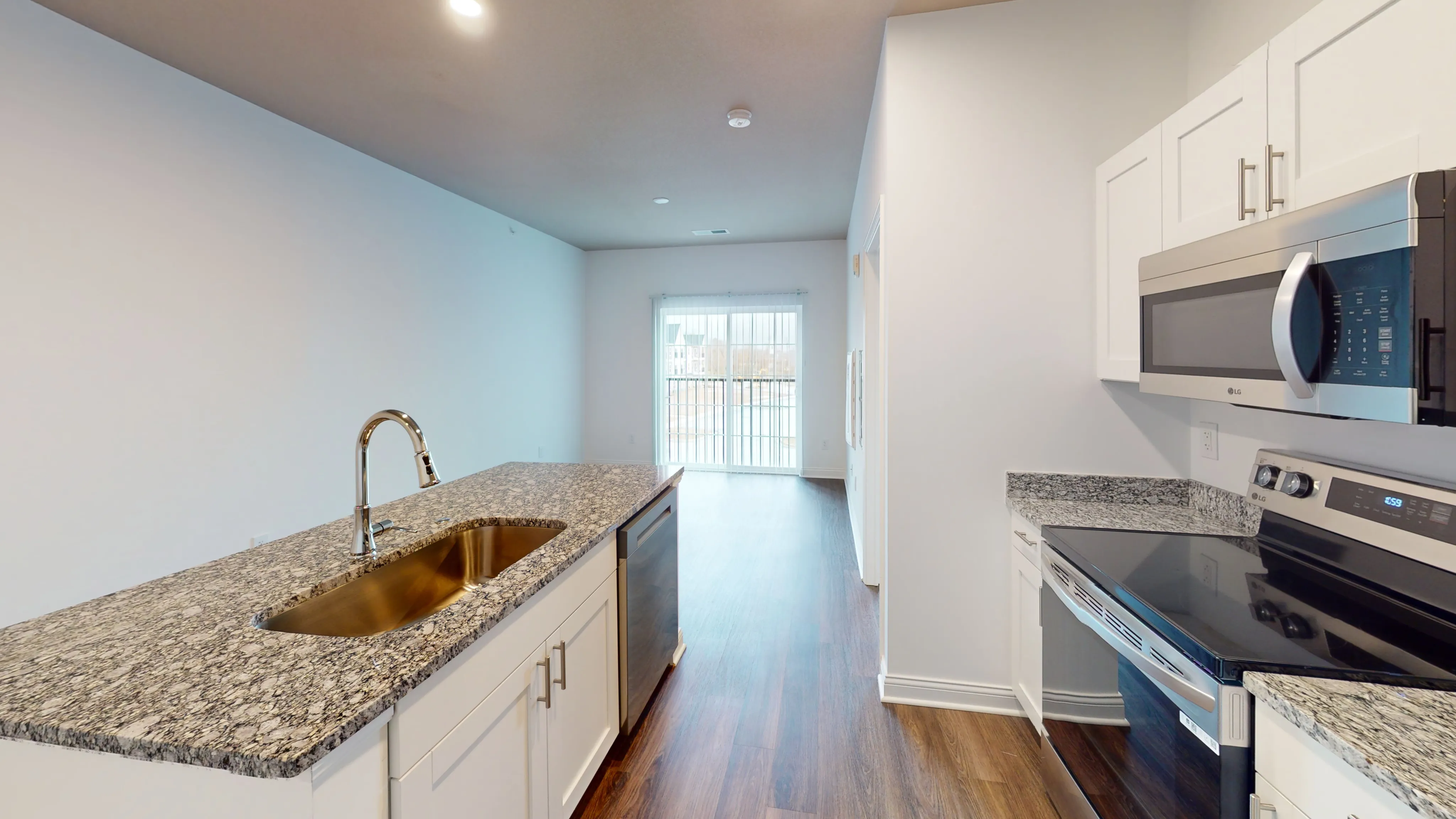 Modern kitchen space with elegant granite countertops, stainless steel appliances, and a gleaming wood floor extending to a bright living area with natural light.