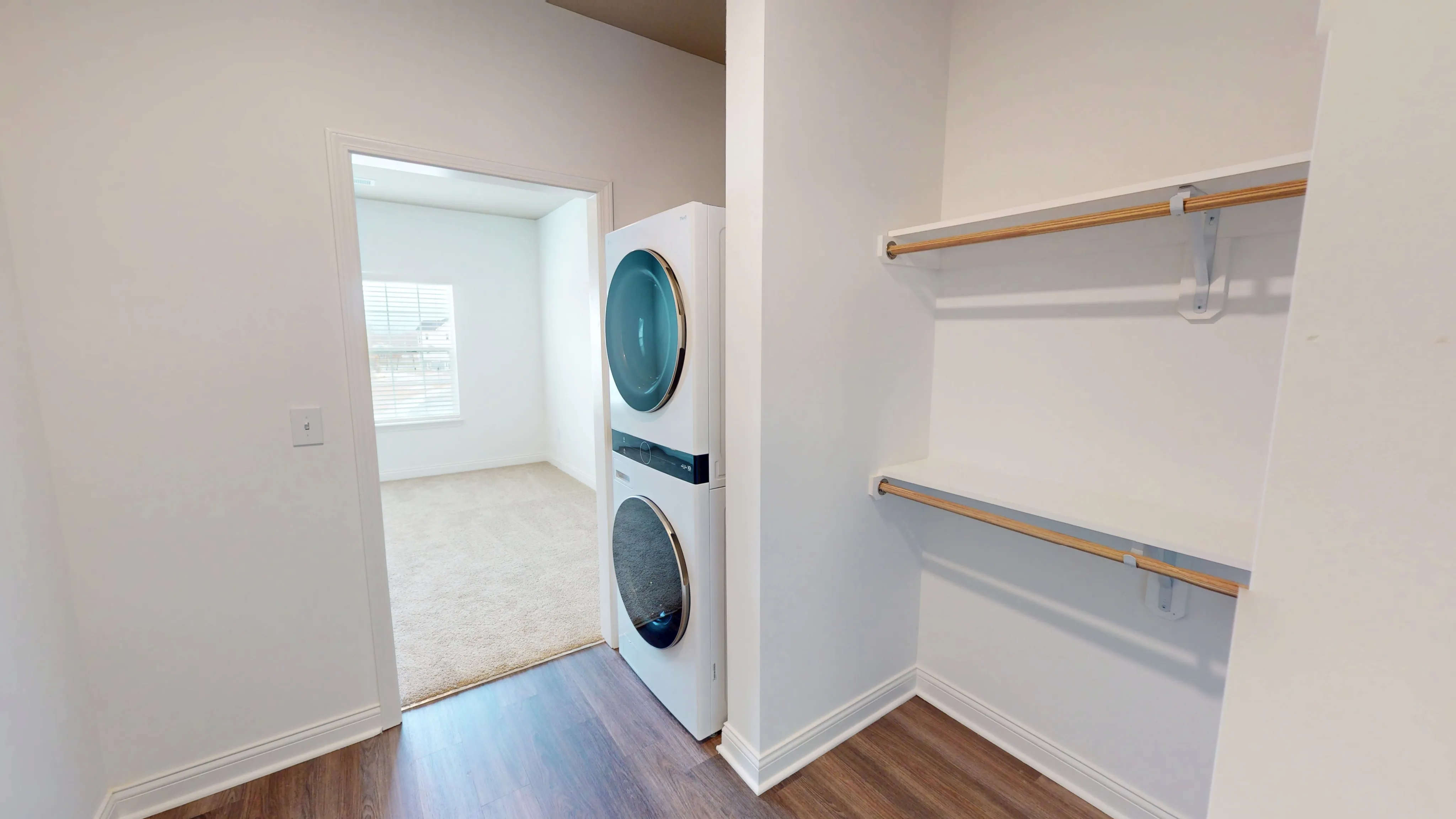 Bright utility room with modern stacked washer and dryer, adjacent to a spacious carpeted bedroom.