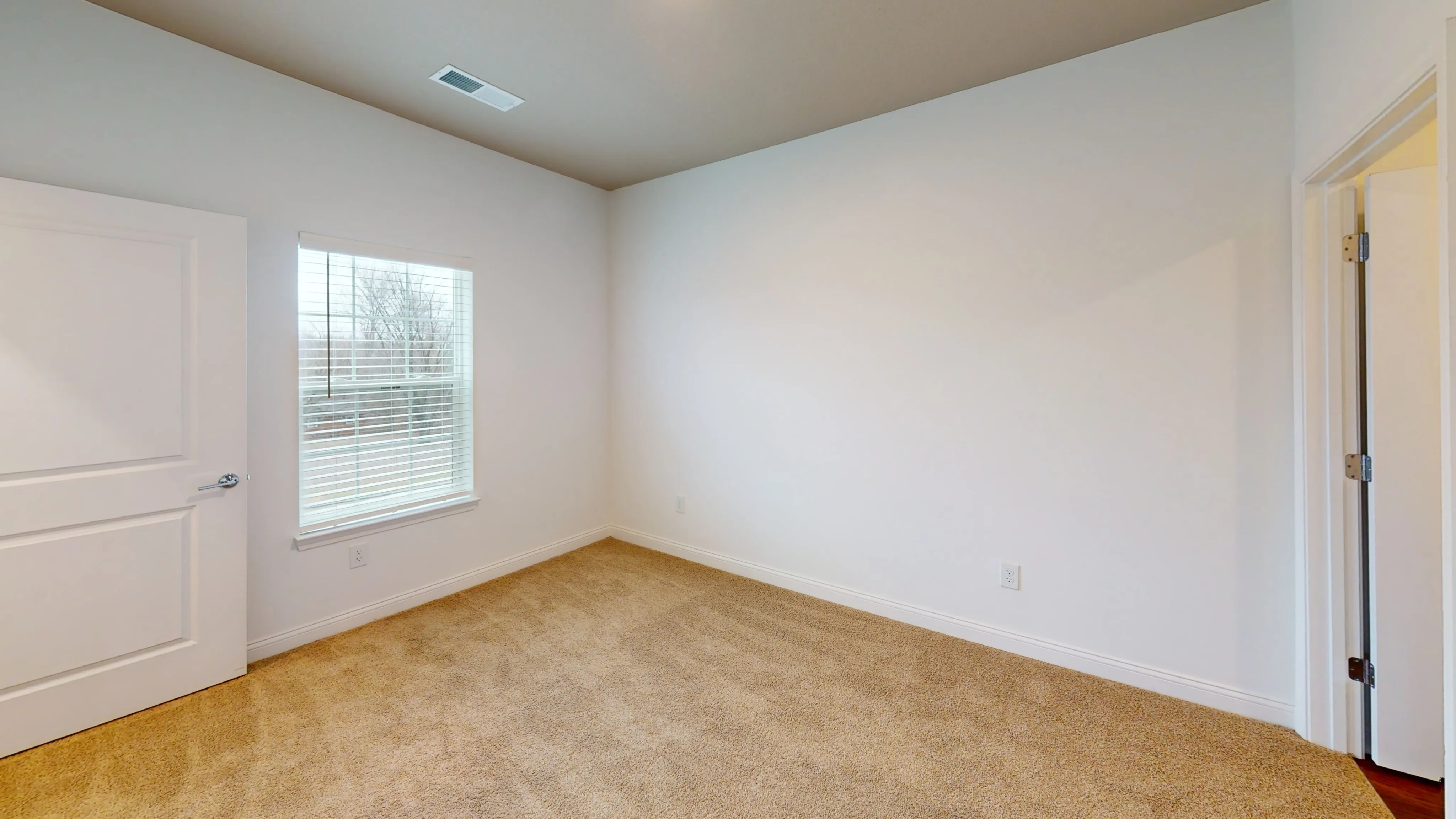 Bright and inviting empty room featuring beige carpet, a large window with blinds, and fresh white walls.