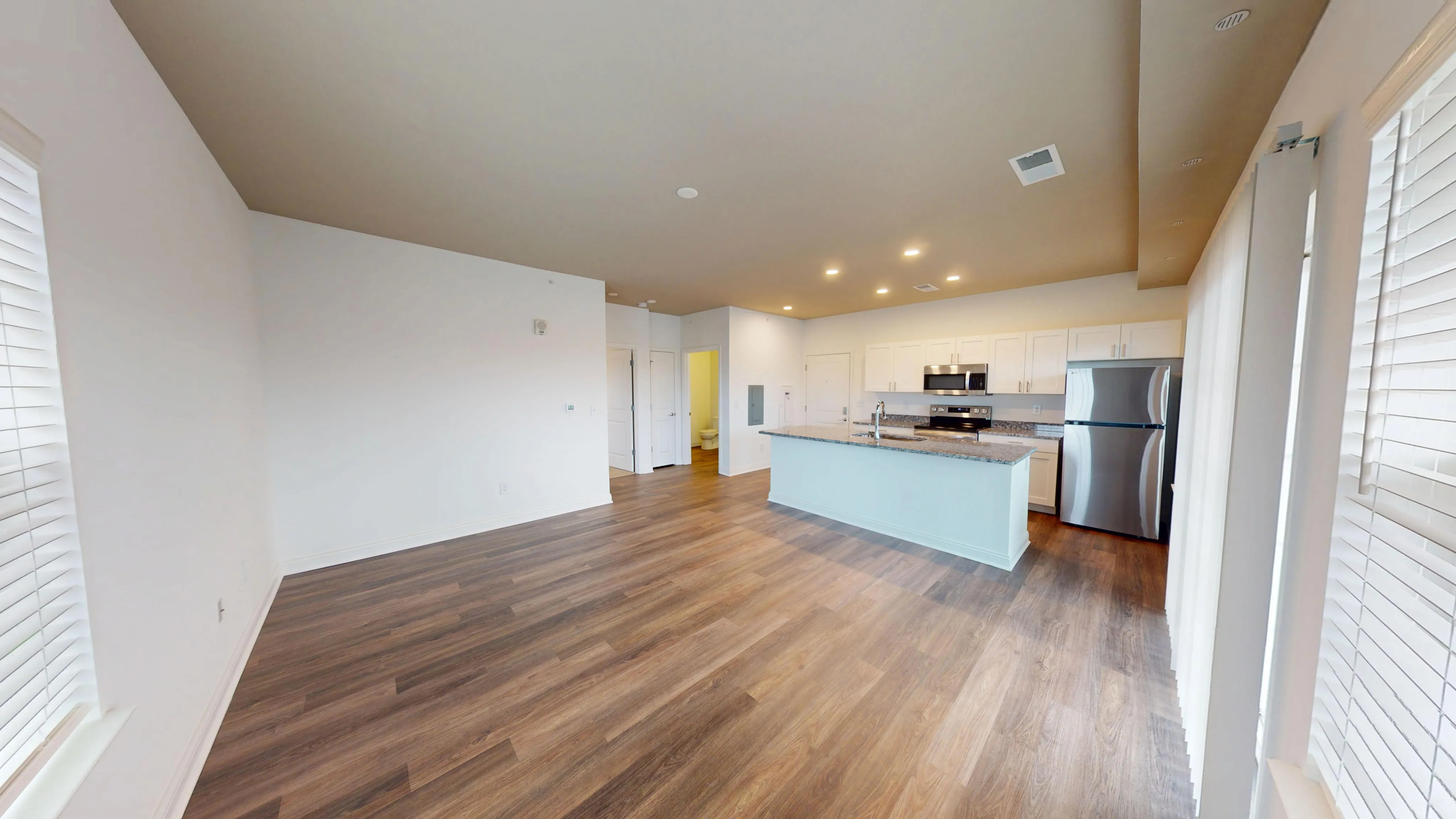 Modern open-concept living space featuring elegant hardwood floors, a sleek kitchen island, and stainless steel appliances, filled with natural light.