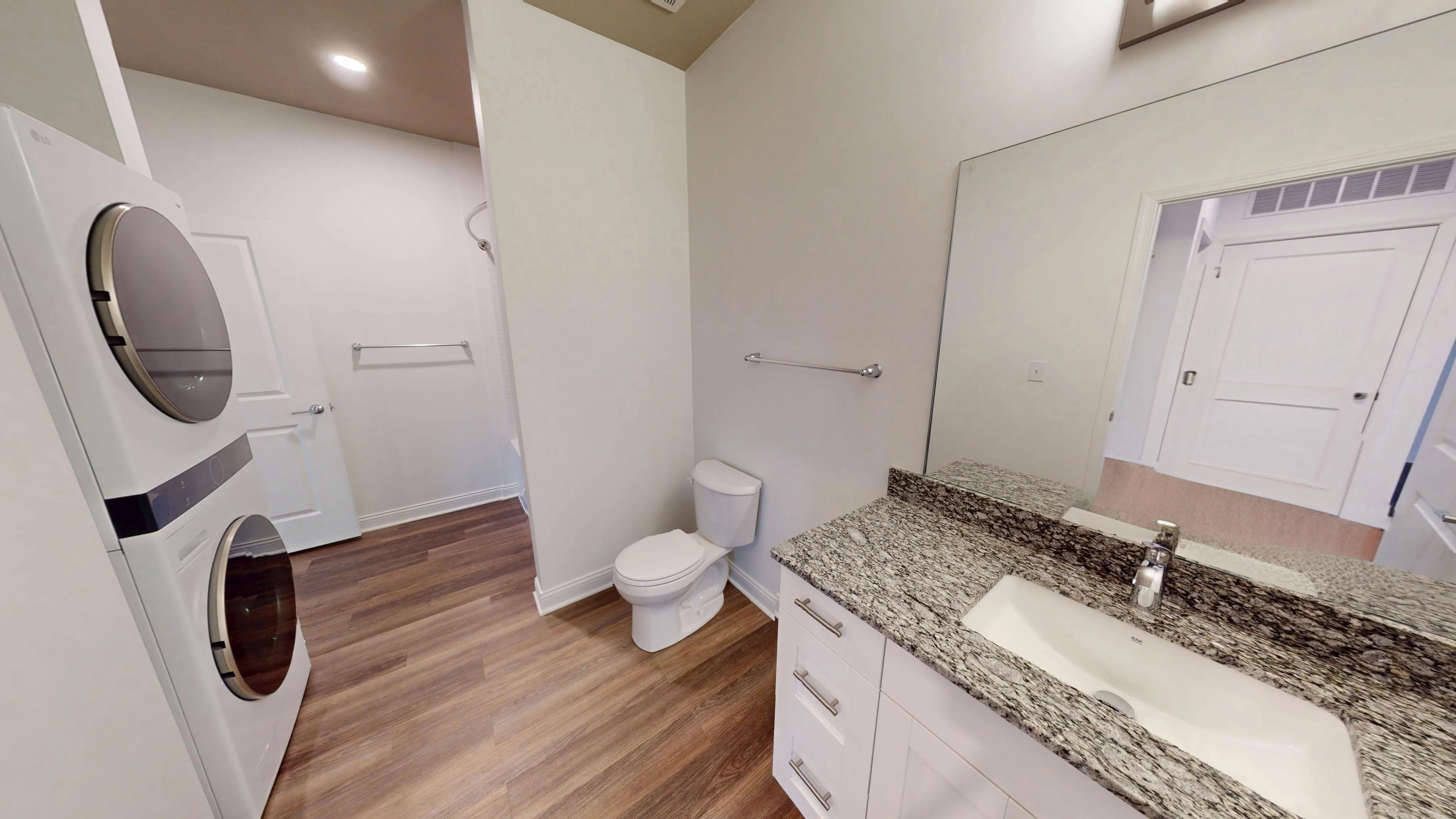 Modern bathroom with granite countertops, elegant vanity, and in-unit washer dryer set.