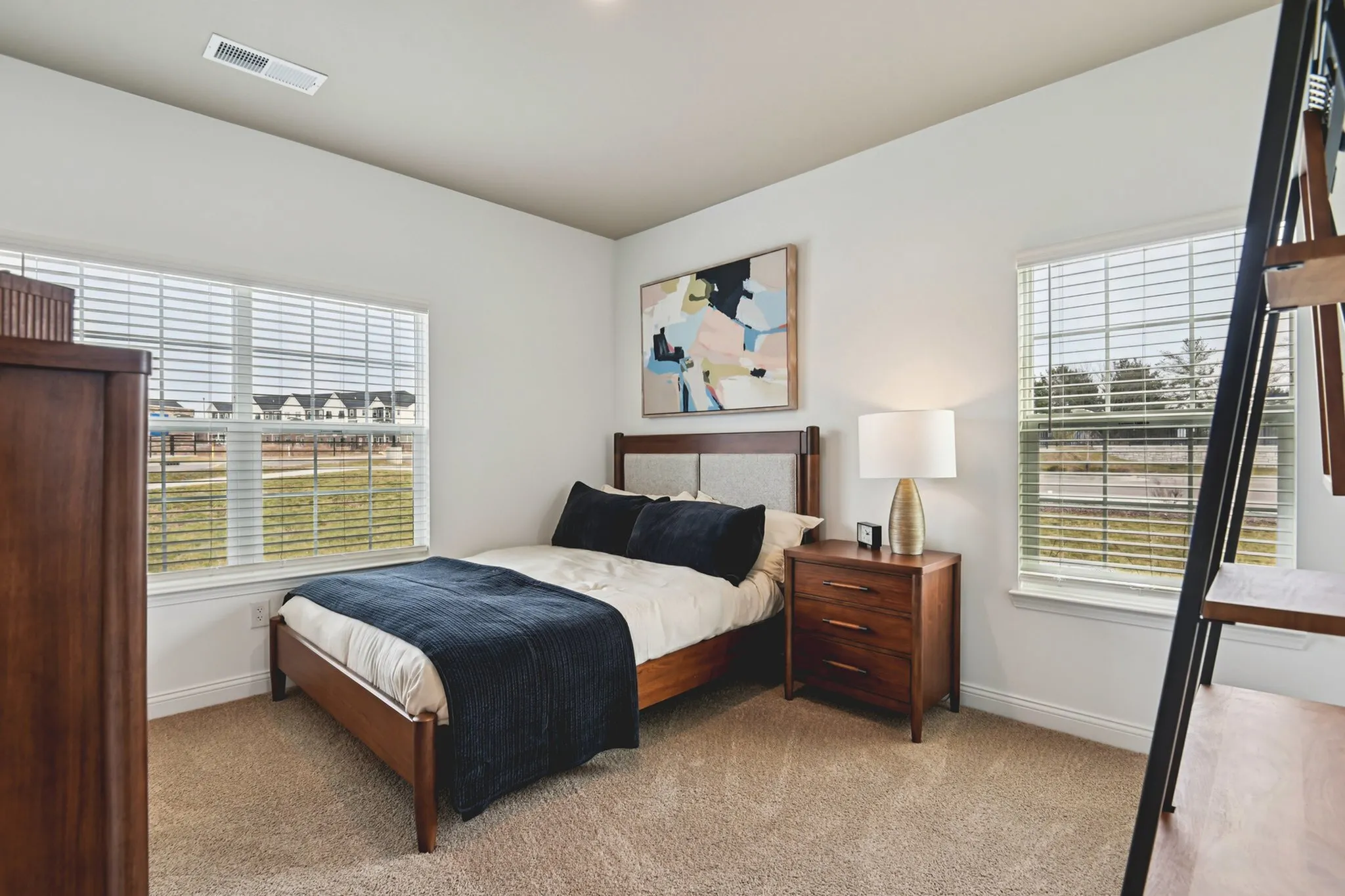 Cozy bedroom with modern wooden furniture, large windows, and abstract wall art, creating a bright and inviting atmosphere.