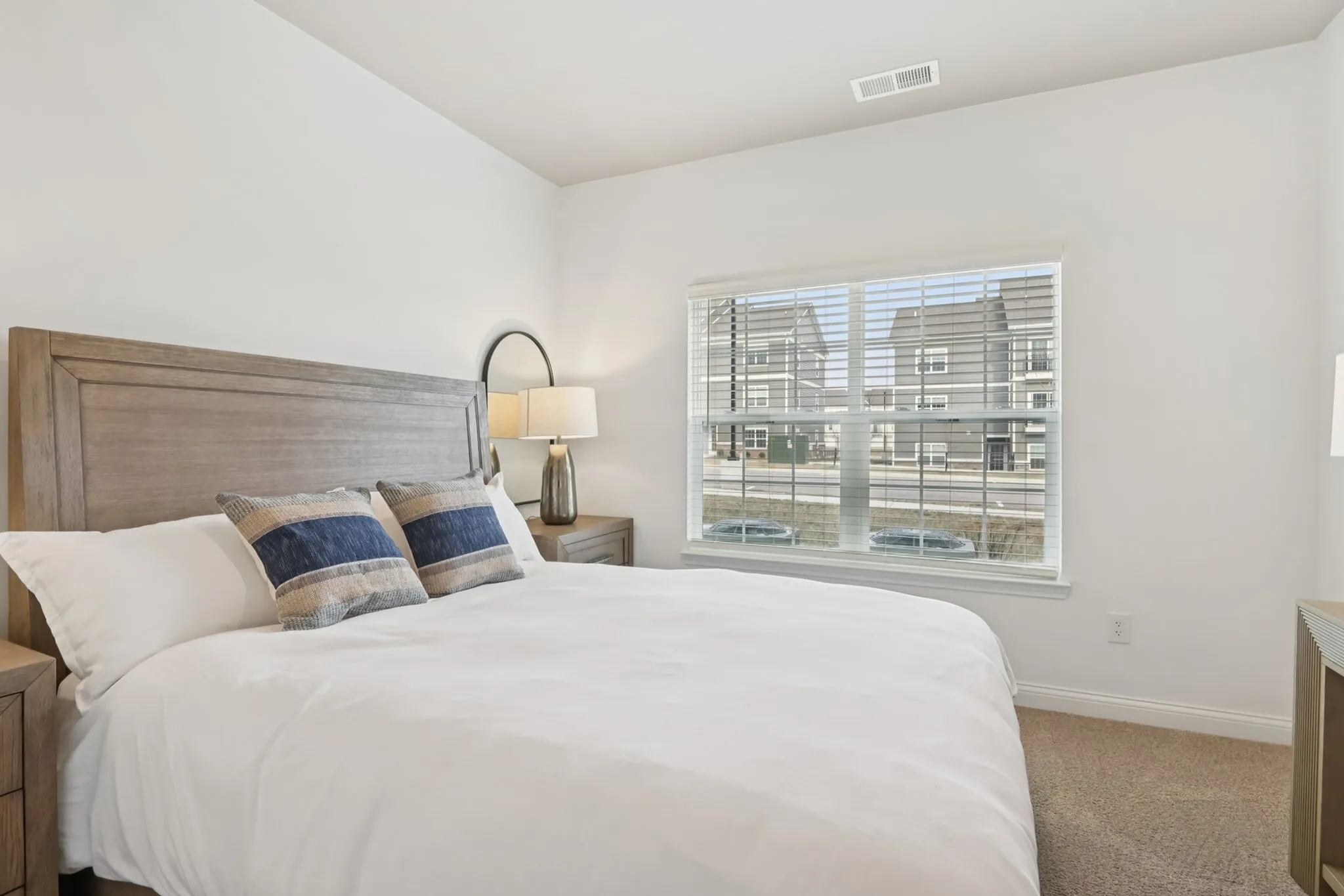 Inviting bedroom with a large window, cozy bedding, elegant wooden headboard, and stylish decor, perfect for relaxation.