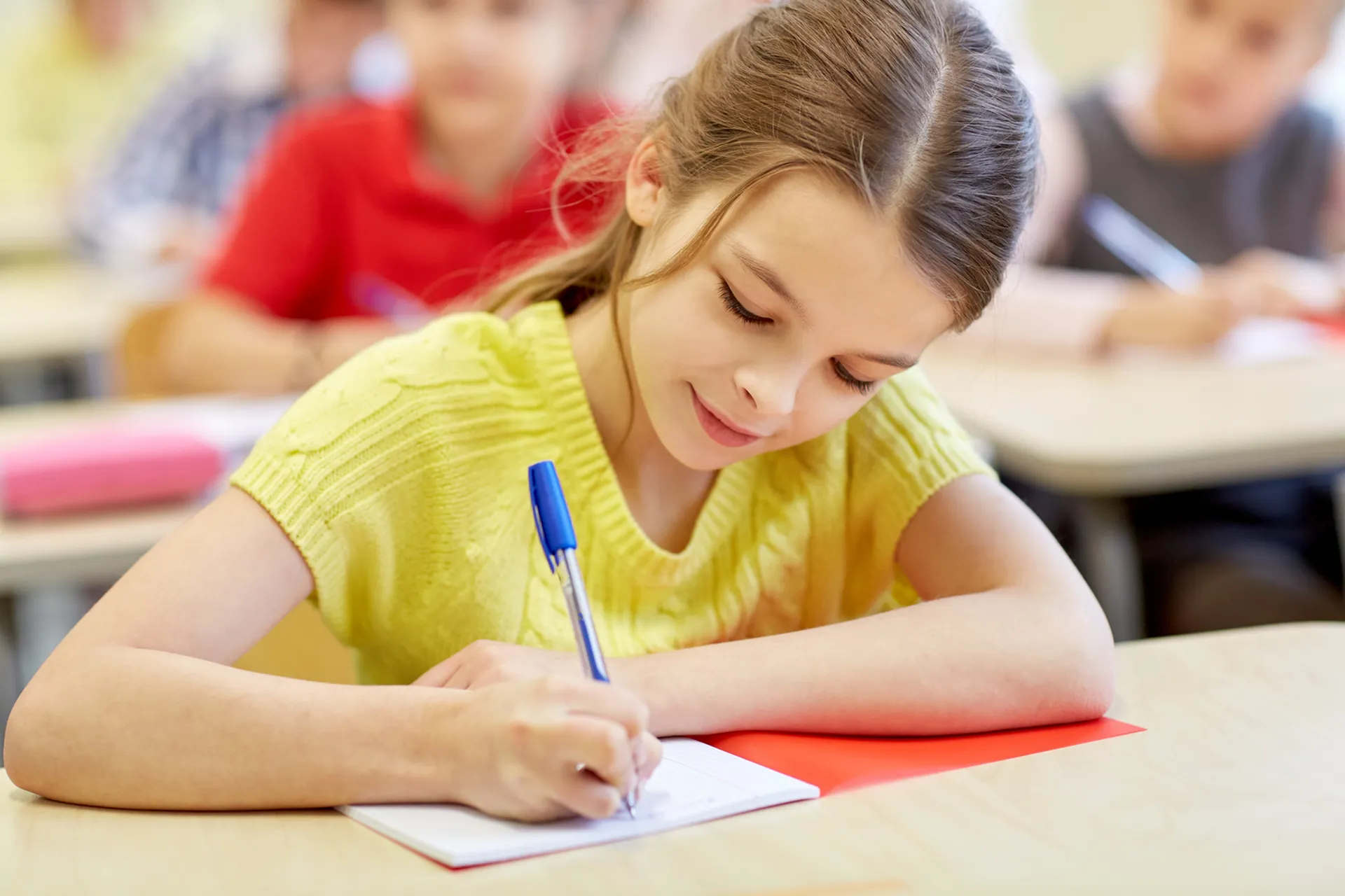 Young student in a bright classroom eagerly writing in a notebook, showcasing a love for learning.