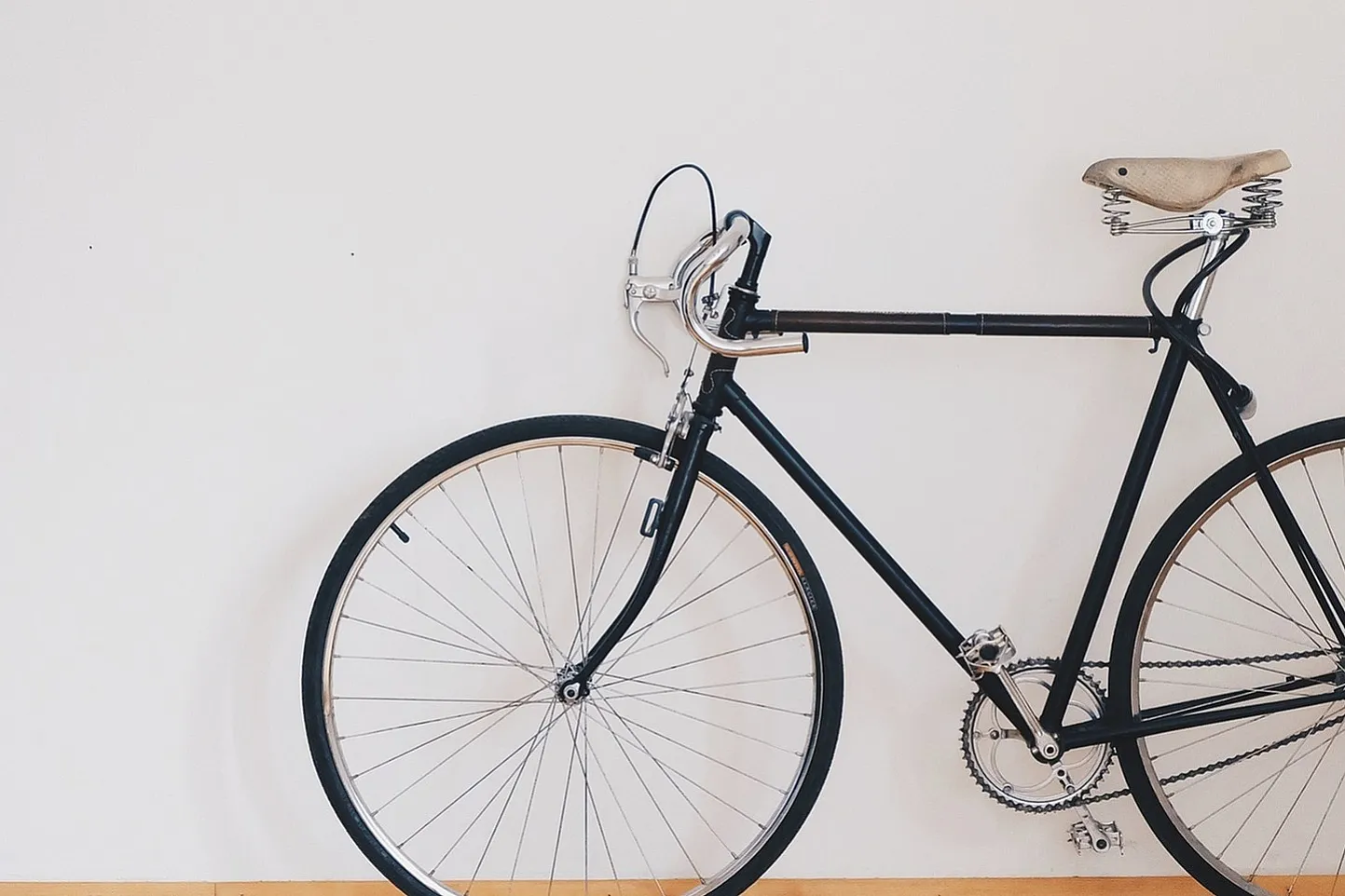 Sleek black bicycle with a vintage touch displayed against a minimalist white wall and wooden floor, accented by a vibrant green plant.