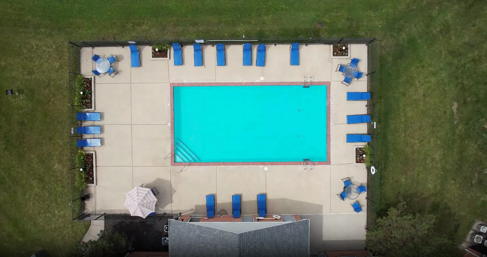 Inviting aerial view of a sparkling blue pool surrounded by blue sun loungers and green lawns, perfect for relaxation.