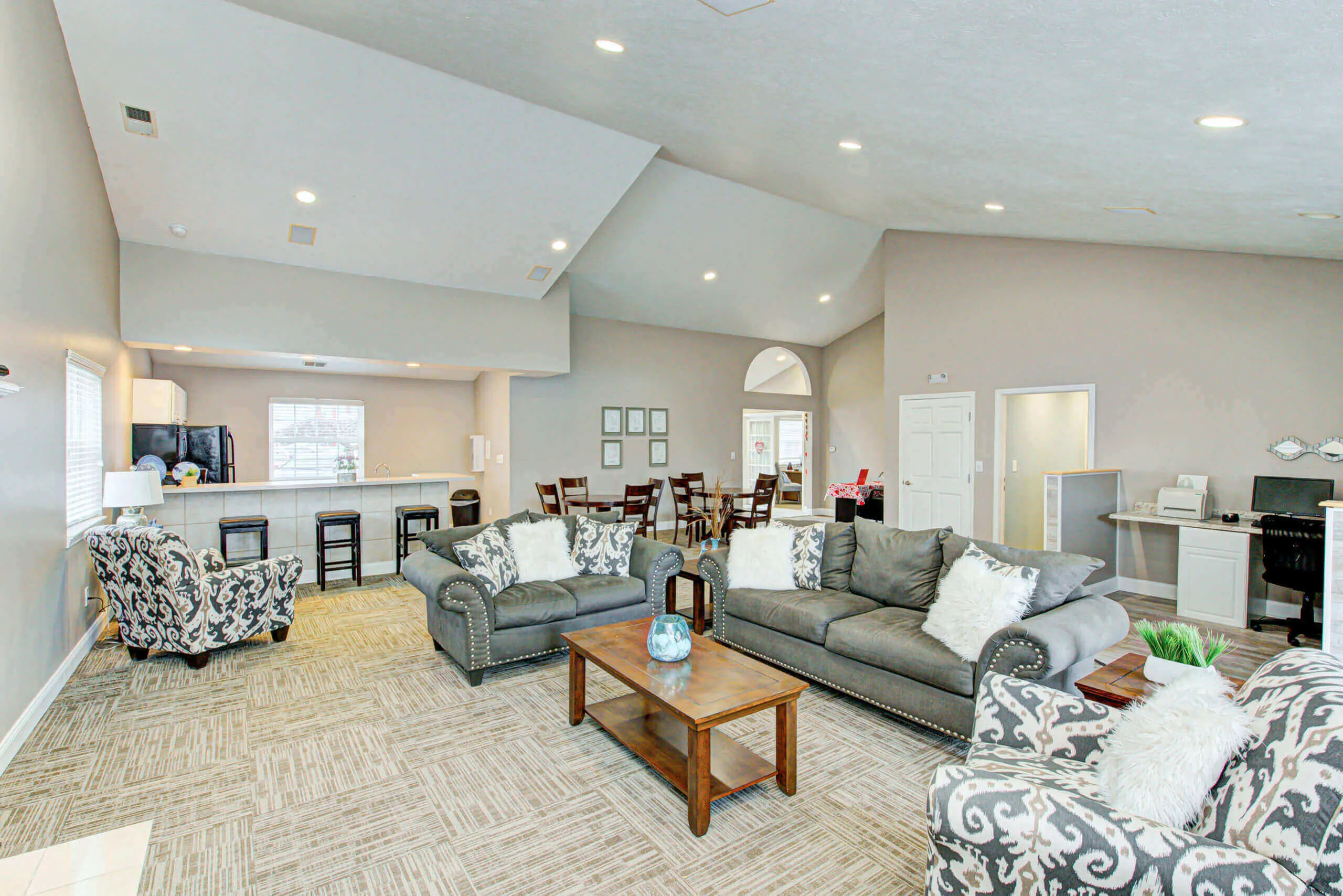 Spacious community lounge with cozy modern seating, high ceilings, and a well-equipped kitchen area.