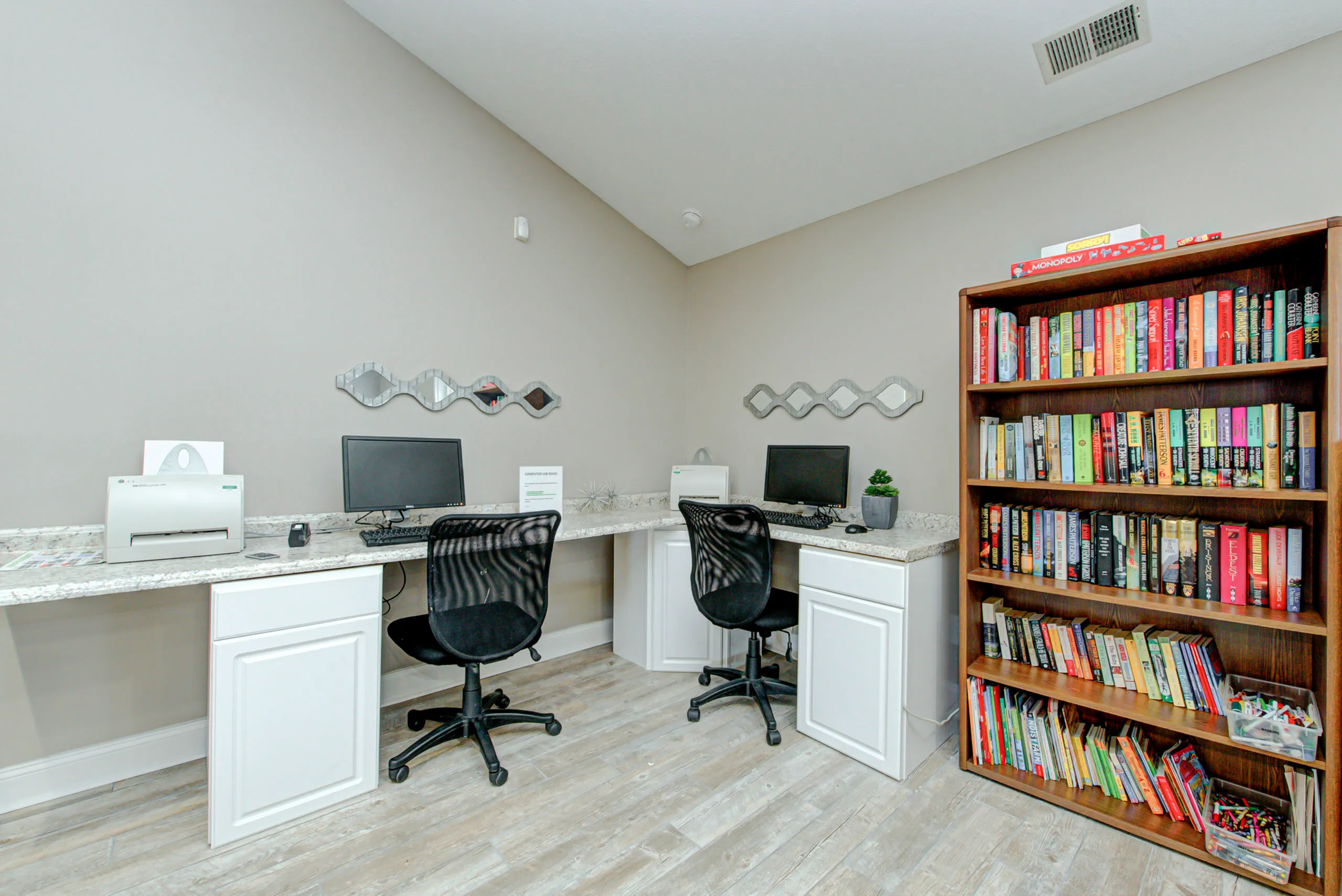 Contemporary home office with dual workstations, sleek granite countertops, stylish shelving, and a vibrant book collection.