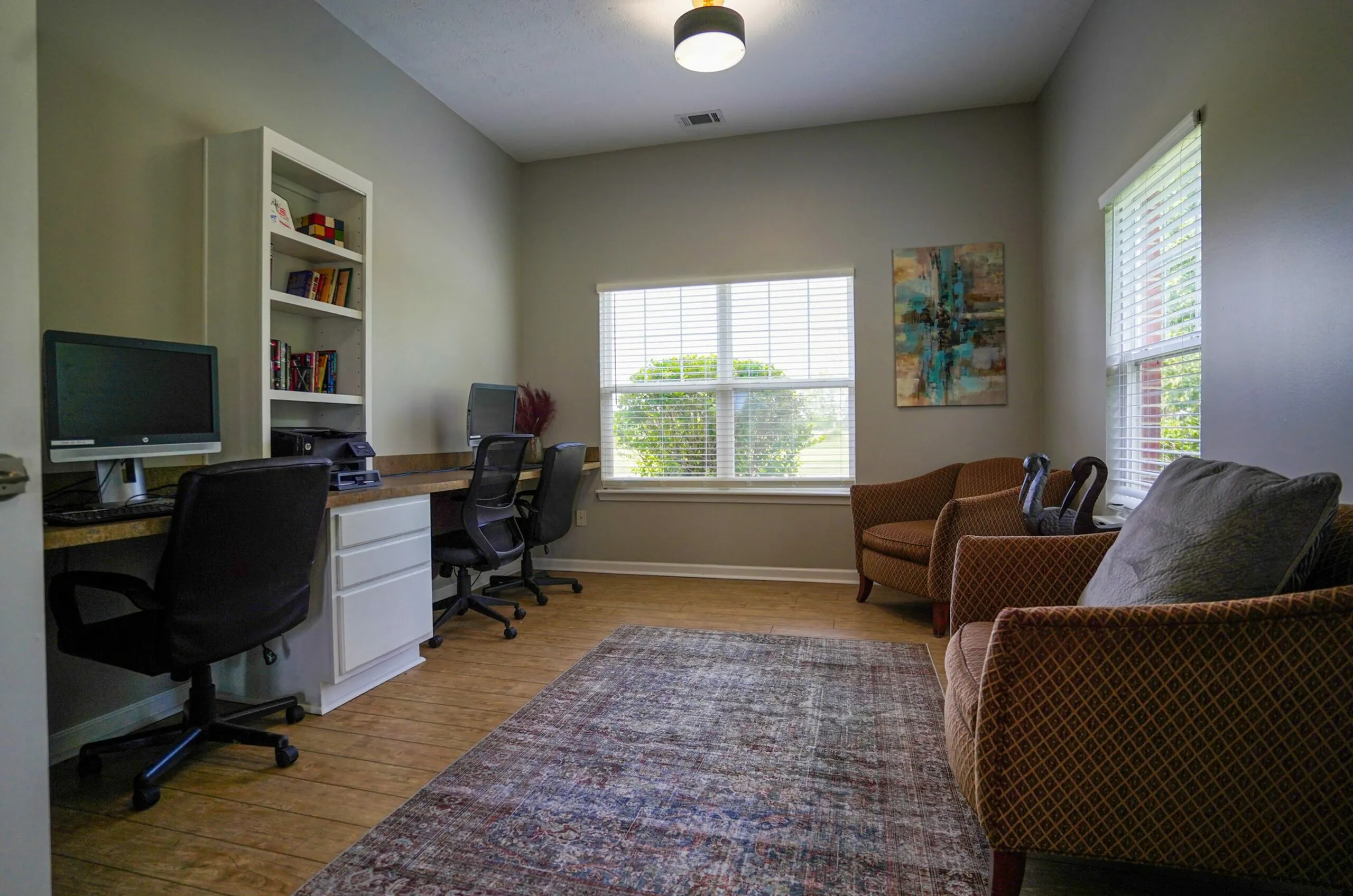 Bright and inviting home office space with dual workstations, modern decor, and ample natural light from large windows.