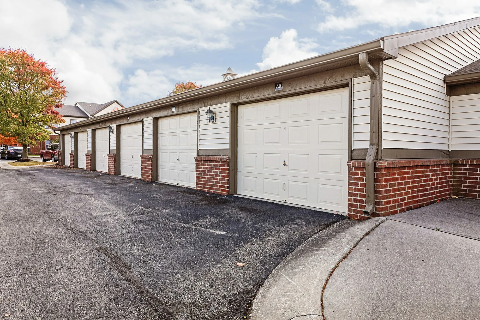 Inviting row of attached garages with charming brick accents, surrounded by autumn trees under a clear sky.