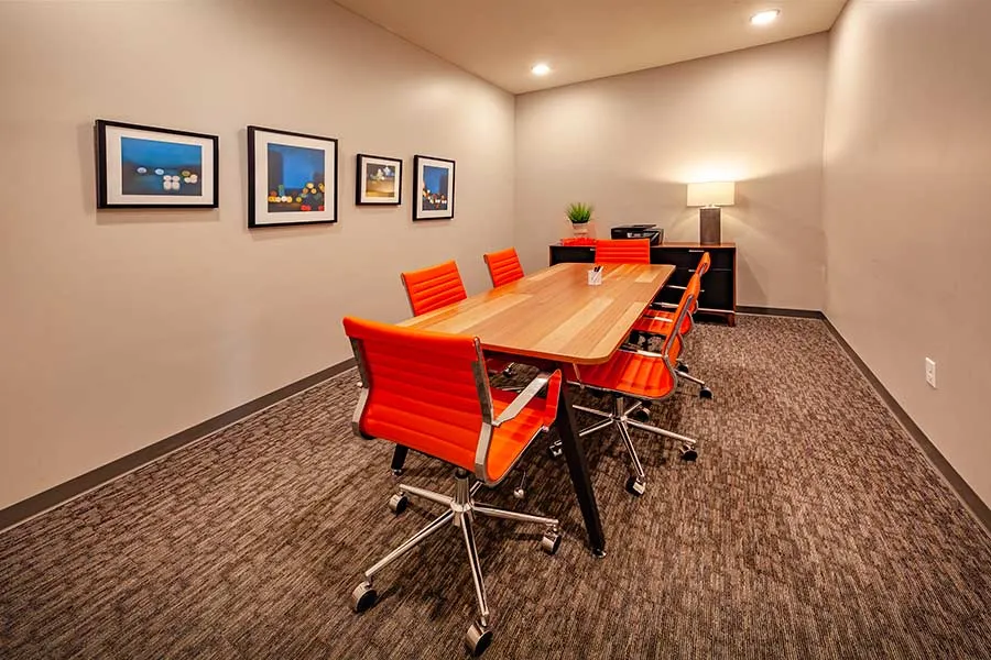 Modern meeting room with vibrant orange chairs, a sleek wooden table, and stylish artwork on the walls.