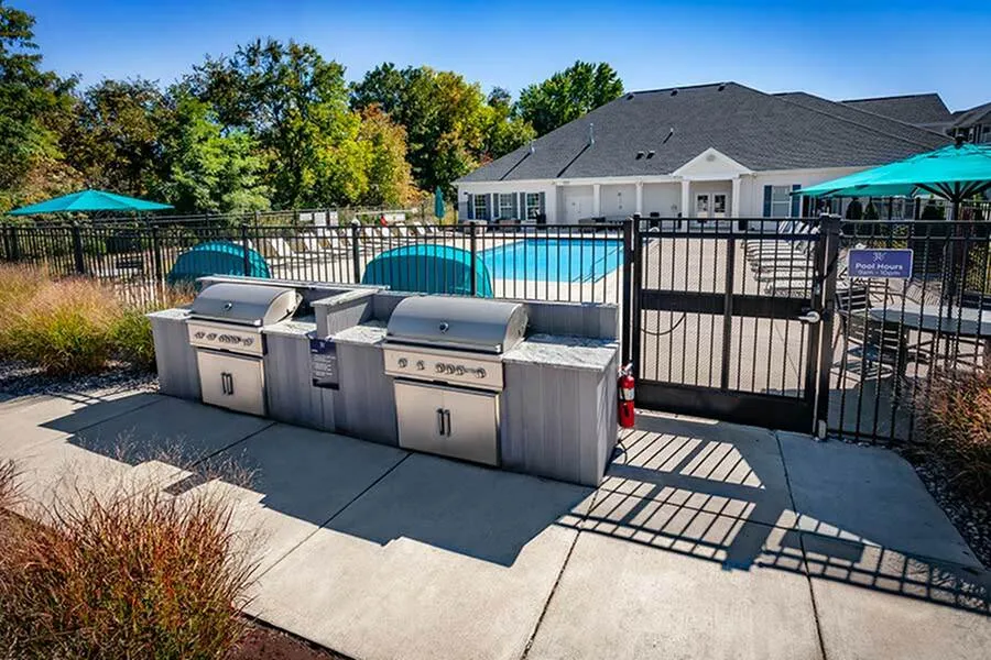 Chic outdoor area showcasing modern grills, a sparkling swimming pool, and vibrant teal umbrellas in a serene residential setting.
