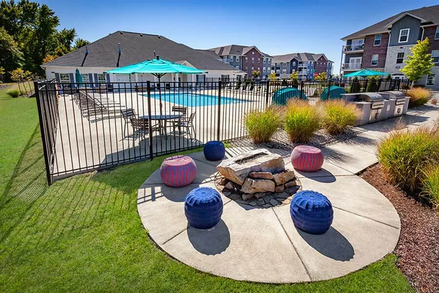 Inviting outdoor space with a sparkling pool, modern lounge chairs, vibrant picnic tables, and a cozy fire pit set in lush greenery.