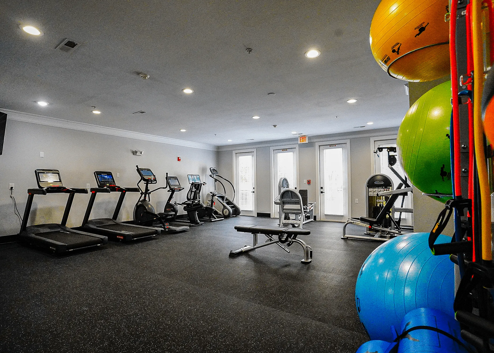 Modern apartment fitness center featuring treadmills, elliptical machines, and vibrant exercise balls in a spacious, well-lit room.